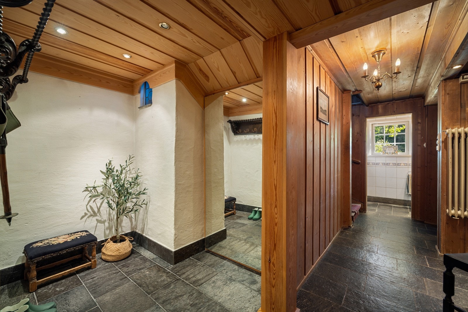 Glimt av hall med skiferflis på gulvet. Tilknyttet hallén er det garderobeløsning til ytterklær og sko. Galleribilde