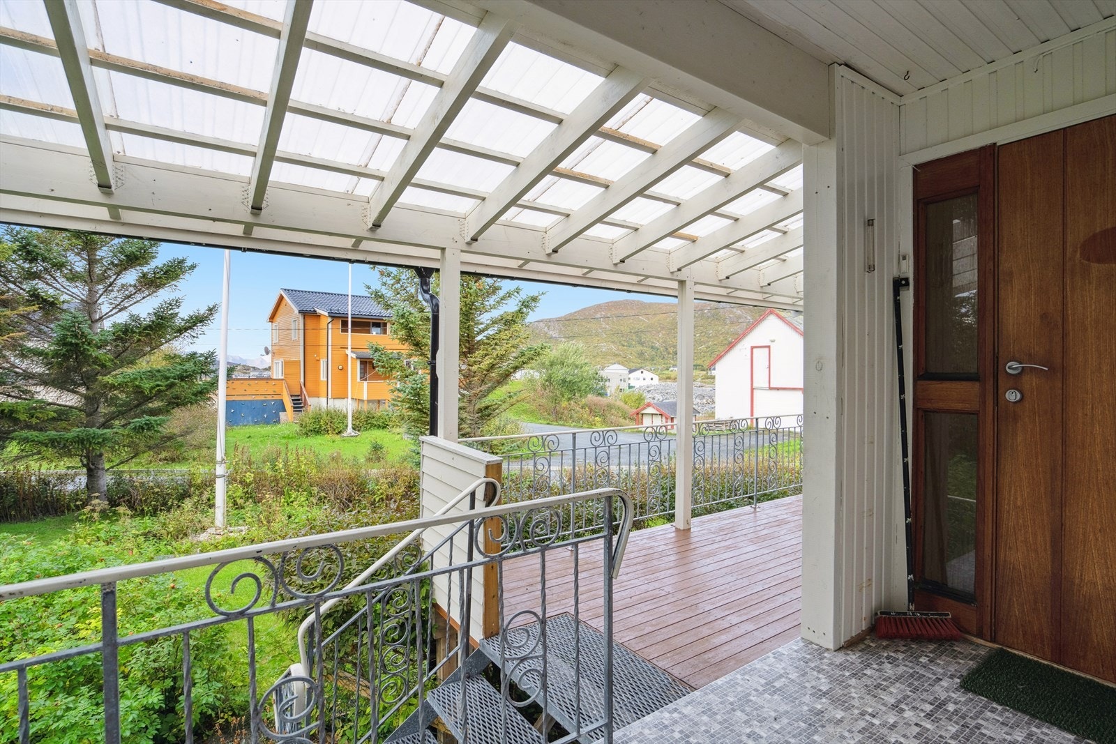 Boligen har et overbygget inngangsparti som gir god beskyttelse mot vær og vind - praktisk i det norske klimaet. Her møtes du av en solid metalltrapp kombinert med en terrasse i trevirke. Galleribilde