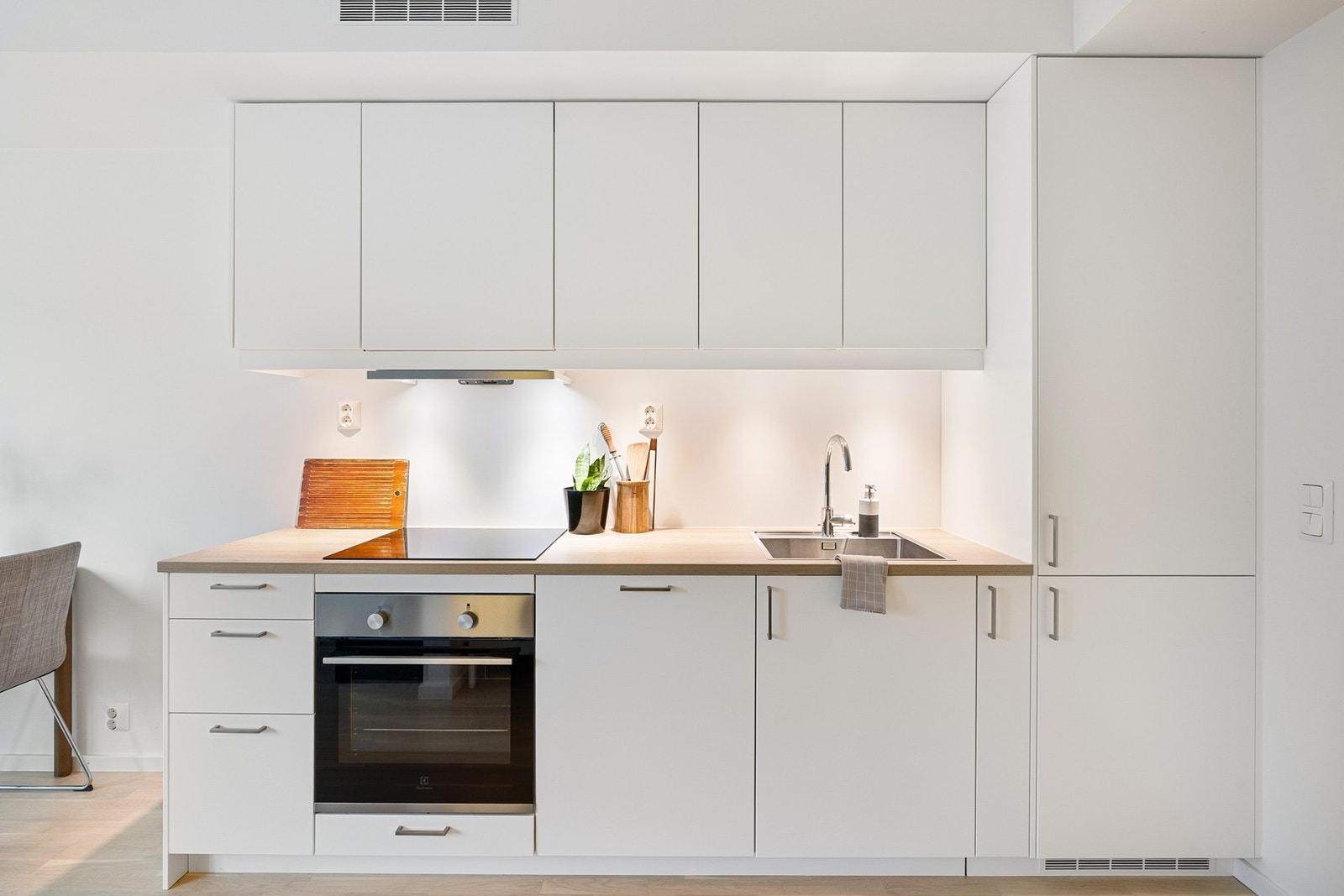 Kjøkkenet har en stilren og moderne utforming med glatte, hvite fronter og benkeplate i varm treimitasjon som gir en fin kontrast. Galleribilde