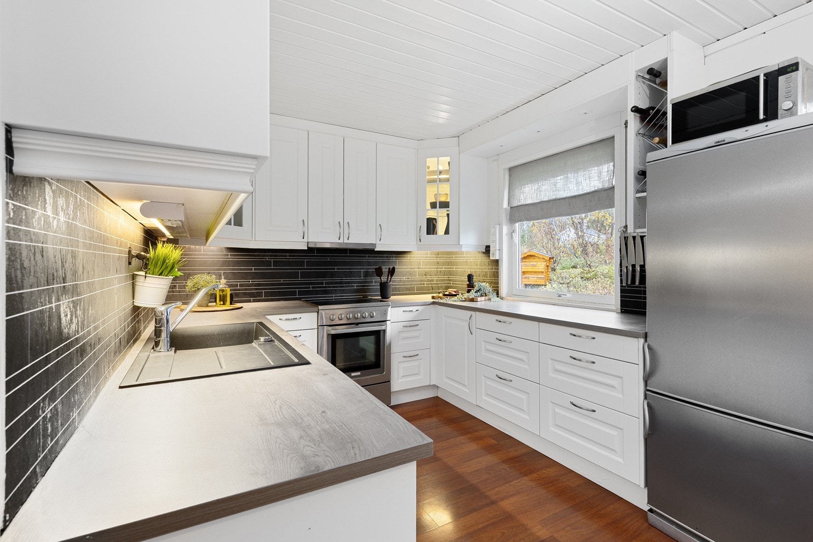 Klassisk kjøkkeninnredning med hvite profilerte fronter. Kjøkkenet har rikelig med skapplass og benkeplass, noe som gir både praktisk oppbevaring og god arbeidsflate til matlaging. Galleribilde