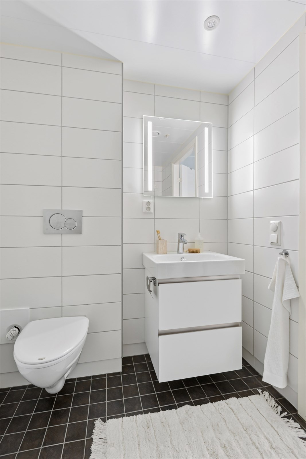 Badet er utstyrt med vegghengt toalett, dusjhjørne med glassvegger, baderomsinnredning med nedfelt servant, samt opplegg for vaskemaskin. Galleribilde