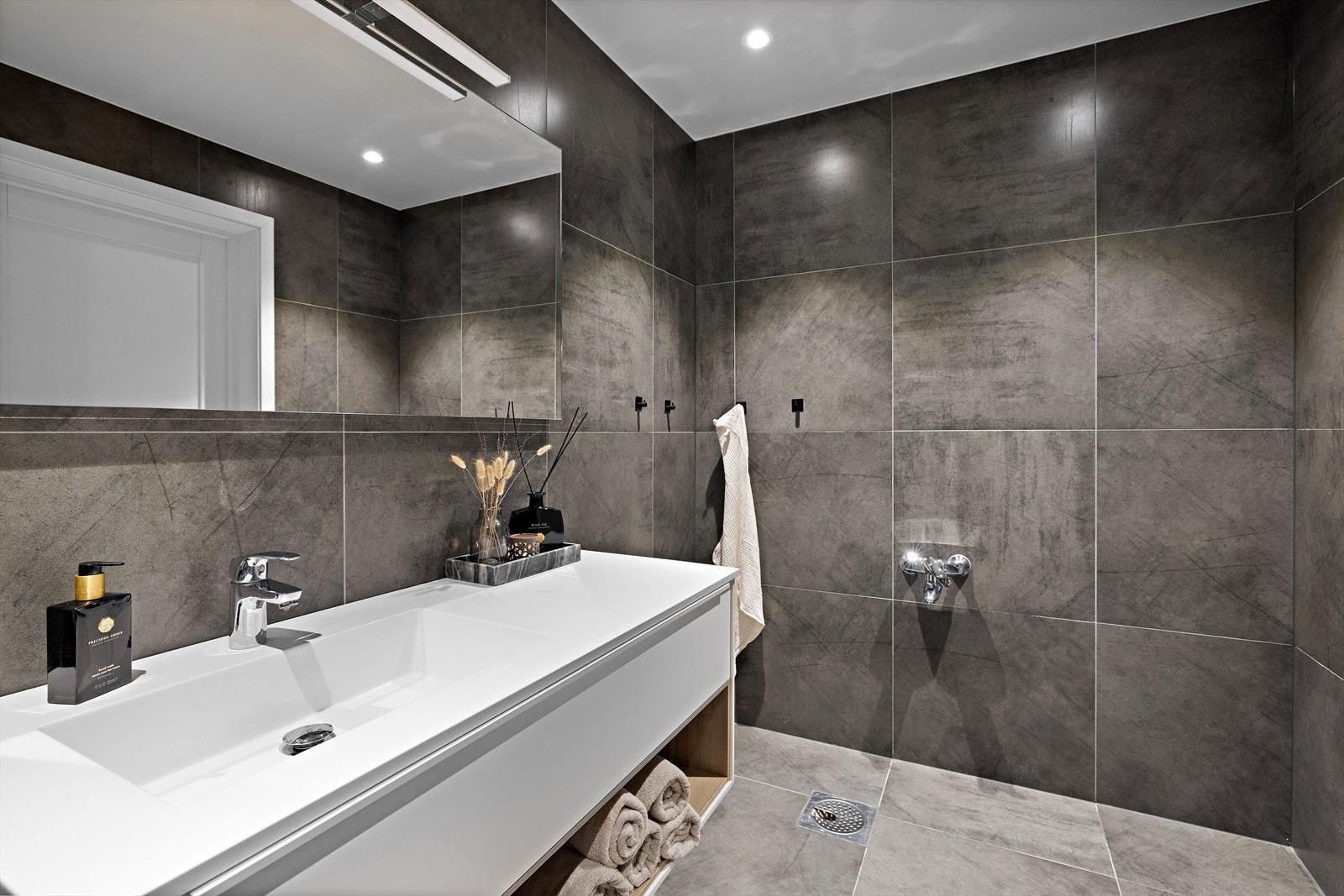 Rommet er innredet med servant i møbel, speil med integrert belysning, veggmontert toalett og dusjhjørne med dusjvegger. Galleribilde