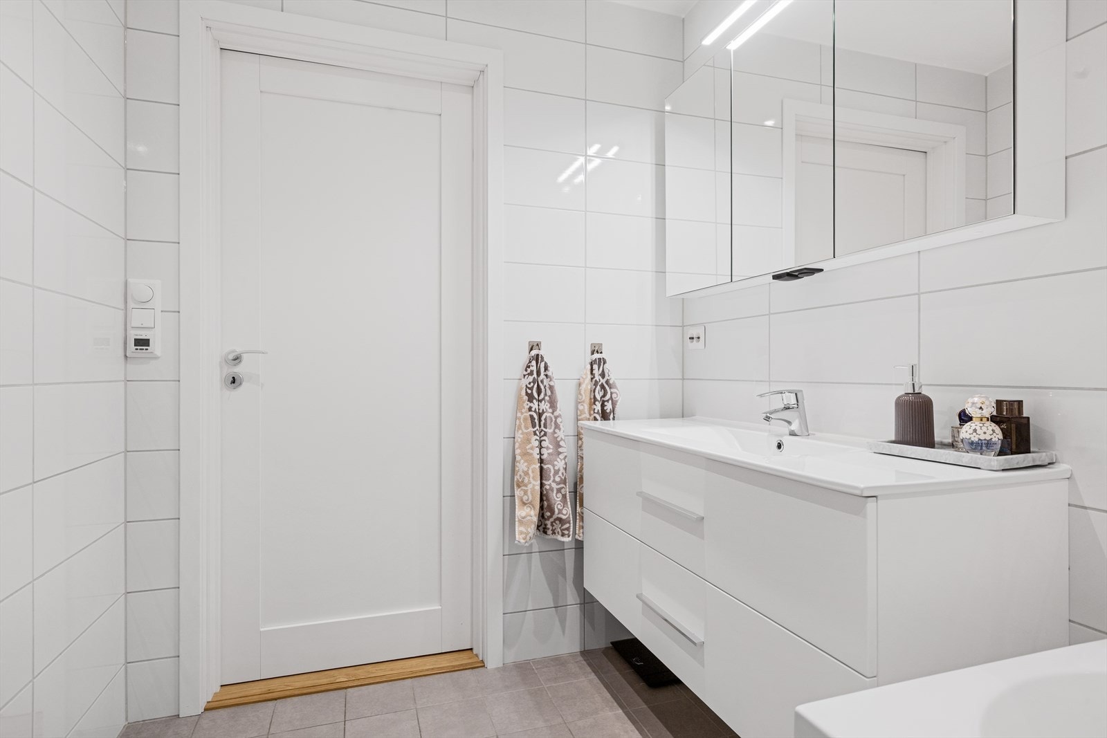 Badet er utstyrt med veggmontert toalett, badekar med dusj og innfellbar glassvegg, innredning med glatte fronter og nedfelt servant, samt speilskap. Galleribilde