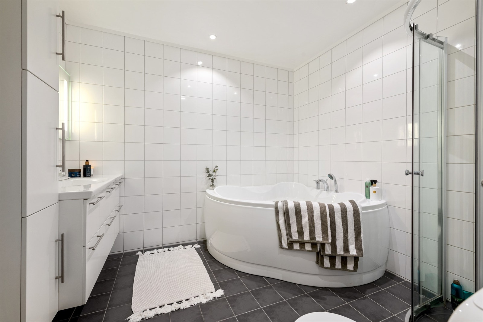 Flislagt bad i underetasjen med stor baderomsinnredning, hjørnebadekar, dusjhjørne og wc Galleribilde