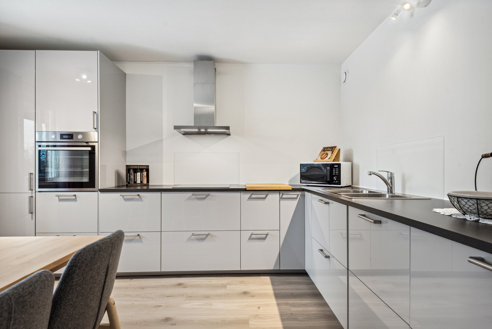 Kjøkkenet har lysmalte vegger og laminat på gulvet. Kjøkkeninnredningen er i en L-formasjon med laminerte skrog, benkeplater og glatte fronter. Galleribilde