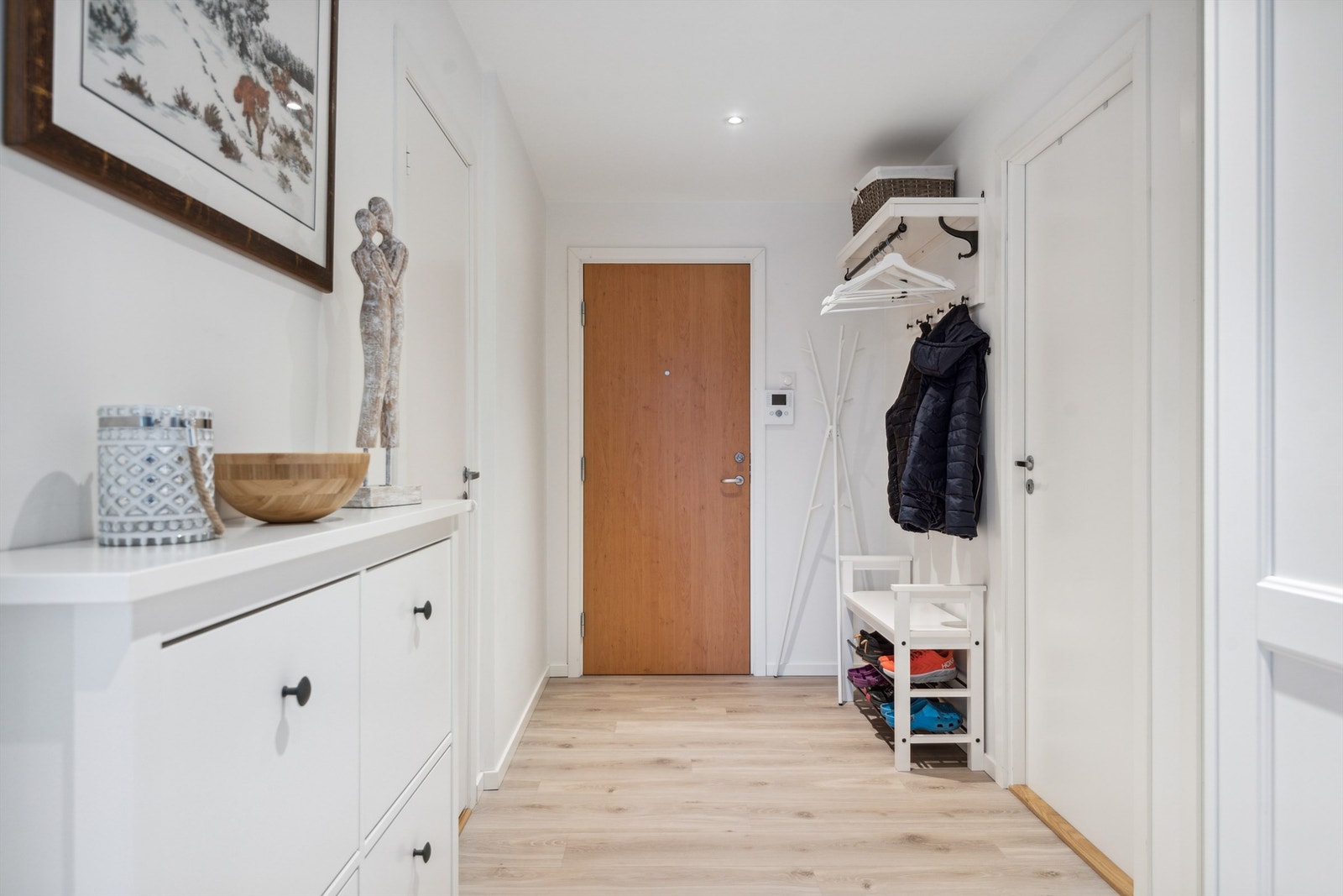 Her kommer man inn i en lys entré med laminat på gulvet og hvitmalte vegger. Her kan man henge fra seg yttertøyet på vegghengte knagger før man vandrer videre inn i leiligheten. Galleribilde