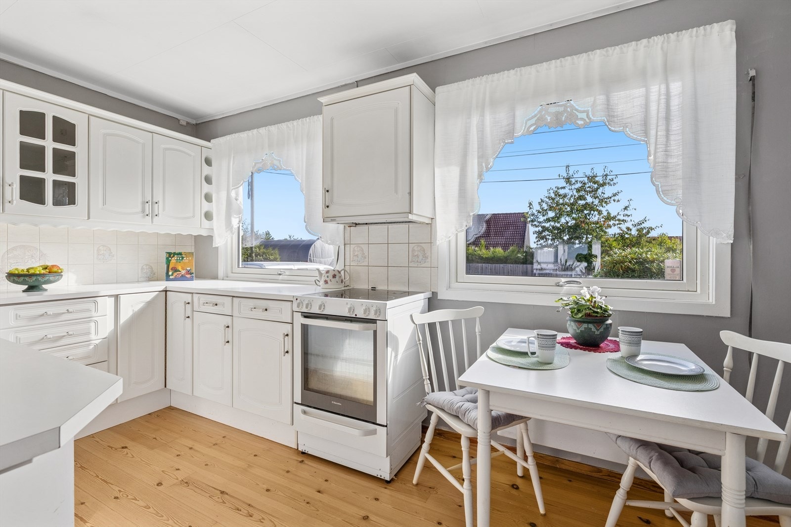 Lyst og koselig kjøkken med mye skap og benkeplass.
Kjøkkenet har innredning fra 1990 med hvite profilerte fronter og laminat benkeplate. Galleribilde