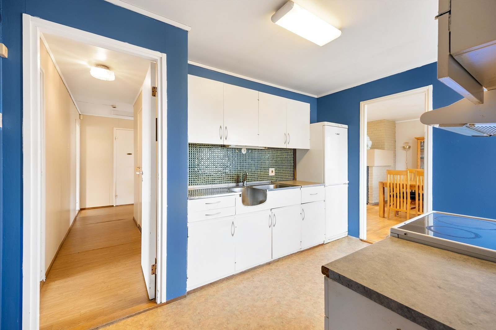 Innredningen består av hvite/glatte fronter, mørk benkeplate med laminatbelegg, fliser mellom skap og vask. Galleribilde