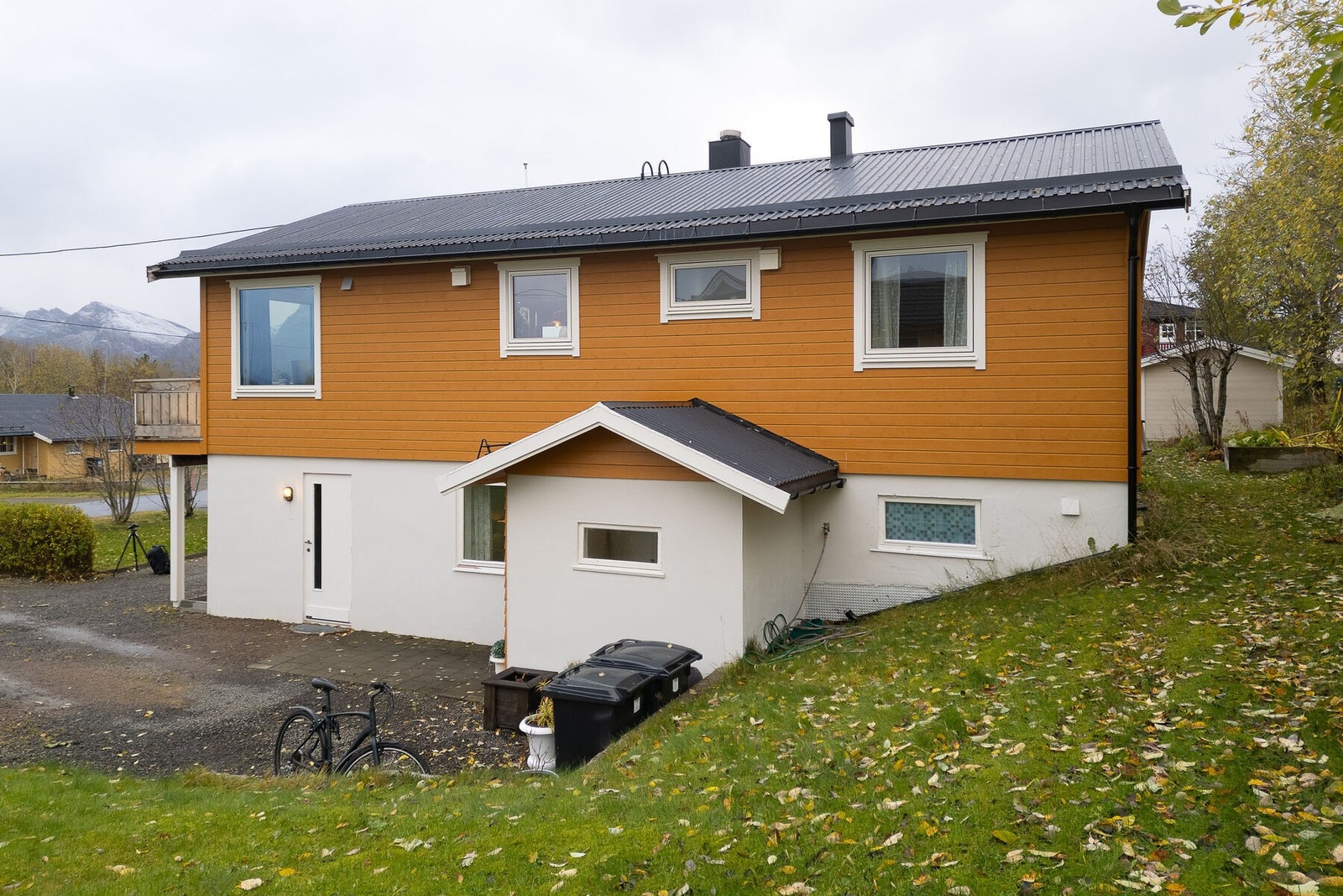 Boligen ligger på en lett skrående tomt med plen, busker og trær. Galleribilde