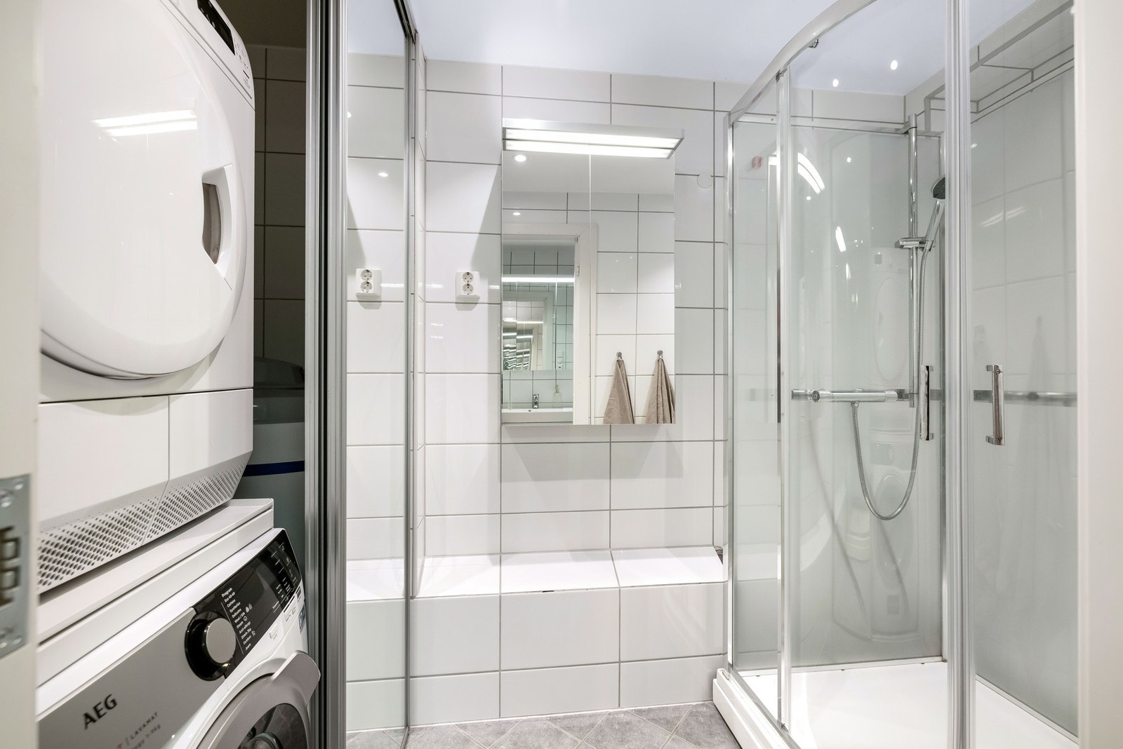 Rommet er innredet med dusjkabinett med skyvedører i glass, servant og opplegg for vaskemaskin og tørketrommel i praktisk skyvedørsgarderobe. Galleribilde