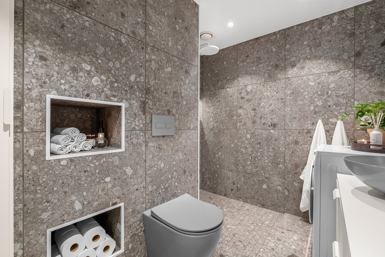 Badet har unike detaljer som veggintegrerte hyller for lagring og grå veggmontert toalett Galleribilde