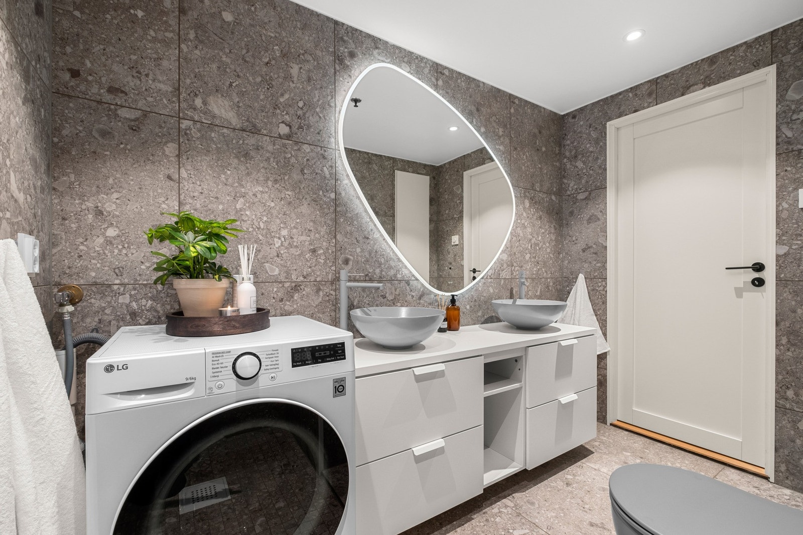 Badet har veggmontert servantinnredning med to stykk toppmonterte servantskåler, veggmontert speil med integrert belysning og opplegg for vaskemaskin Galleribilde