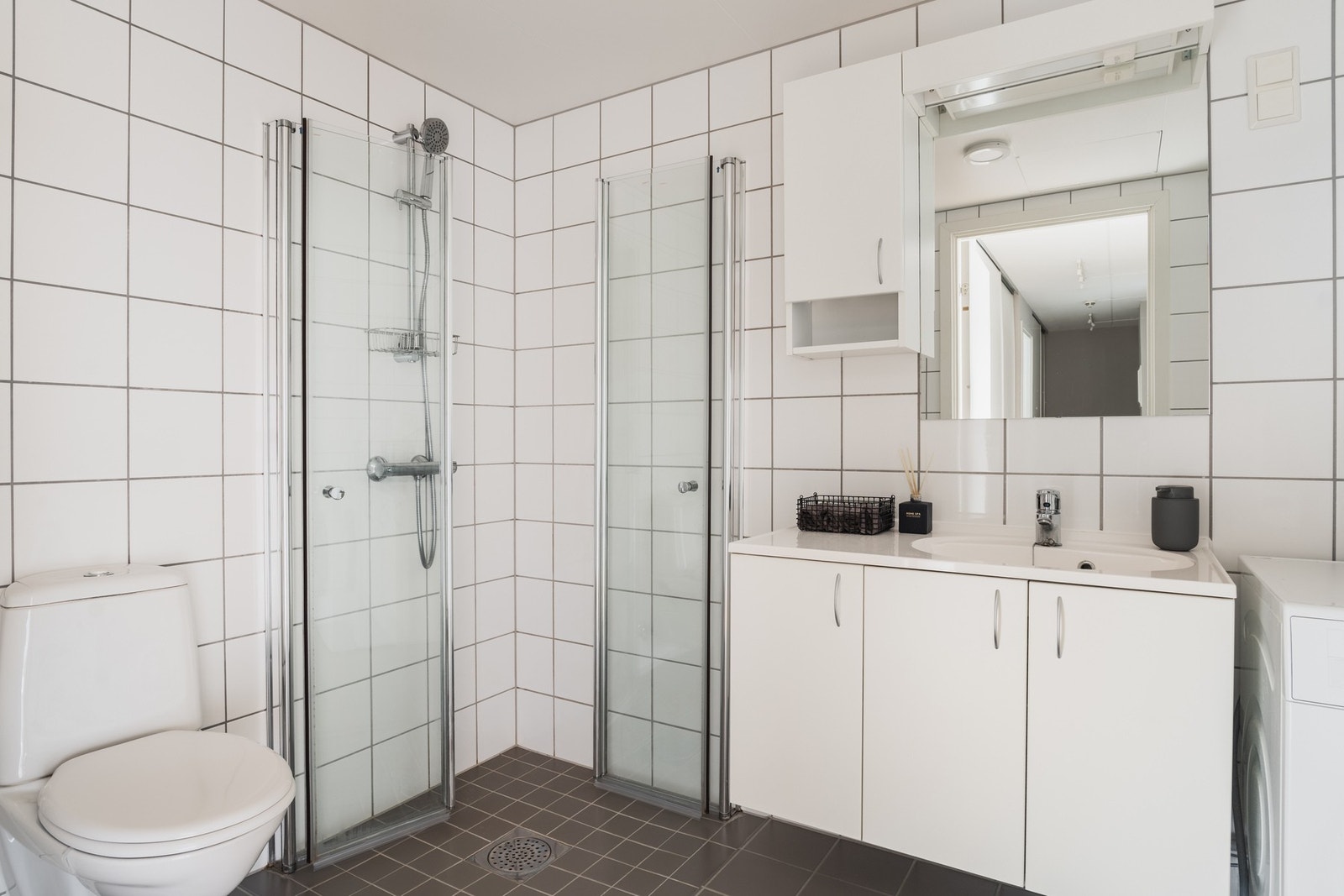 Innredet med innfellbare dusjdører i herdet glass, vegghengt toalett, romslig baderomsinnredning og vegghengt skap for ekstra lagring. Galleribilde