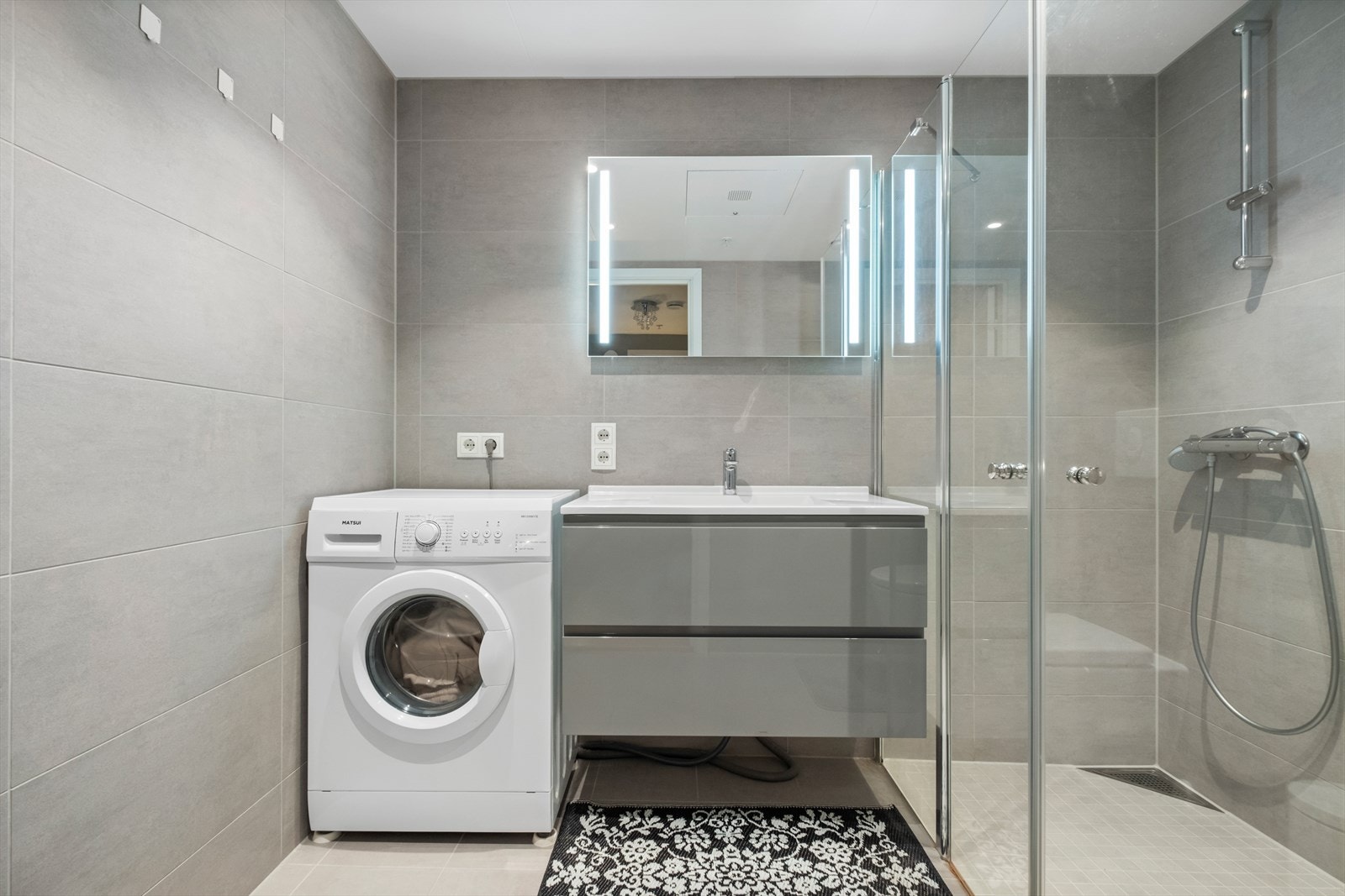 Rommet har innredning med to skuffer og heldekkende servant med etthånds blandebatteri, speil med lys, veggmontert toalett, dusjvegger av glass og opplegg for vaskemaskin. Galleribilde