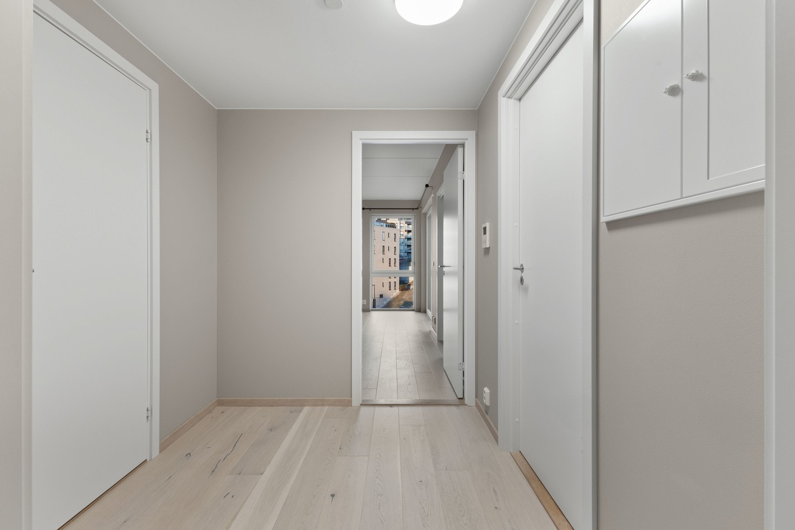 Tiltalende entre/gang med lekker hvitpigmentert parkett på gulv og lysmalte veggflater som gir et godt førsteinntrykk av leiligheten Galleribilde