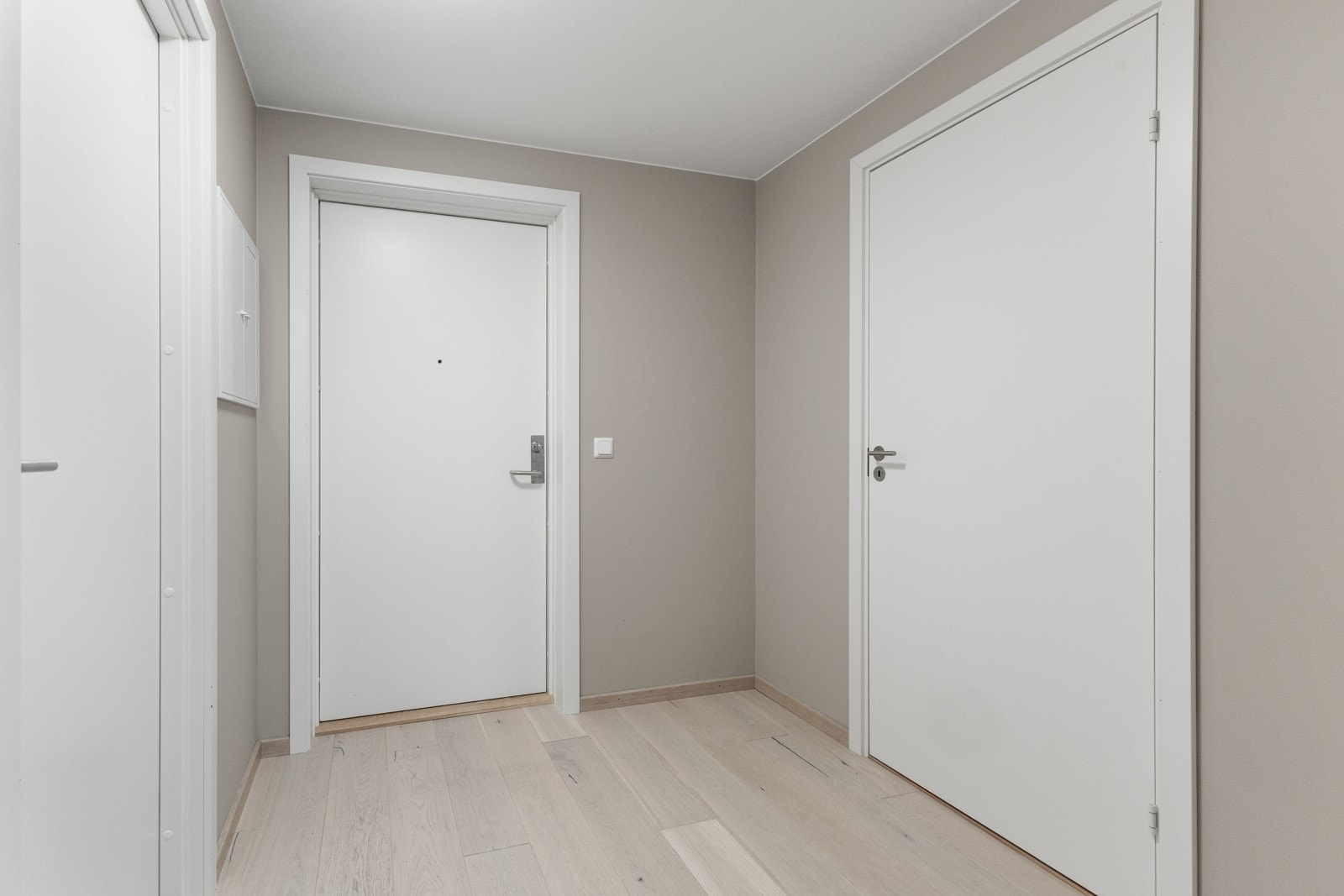 Tiltalende entre/gang med lekker hvitpigmentert parkett på gulv og lysmalte veggflater som gir et godt førsteinntrykk av leiligheten Galleribilde