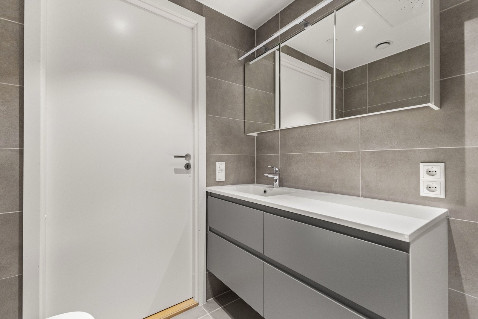 Smakfullt bad nytt i 2023, med flislagte overflater og varme i gulv. Innredningen består av moderne servantmøblement med to skuffer, speil m/integrert belysning og vegghengt toalett. Galleribilde