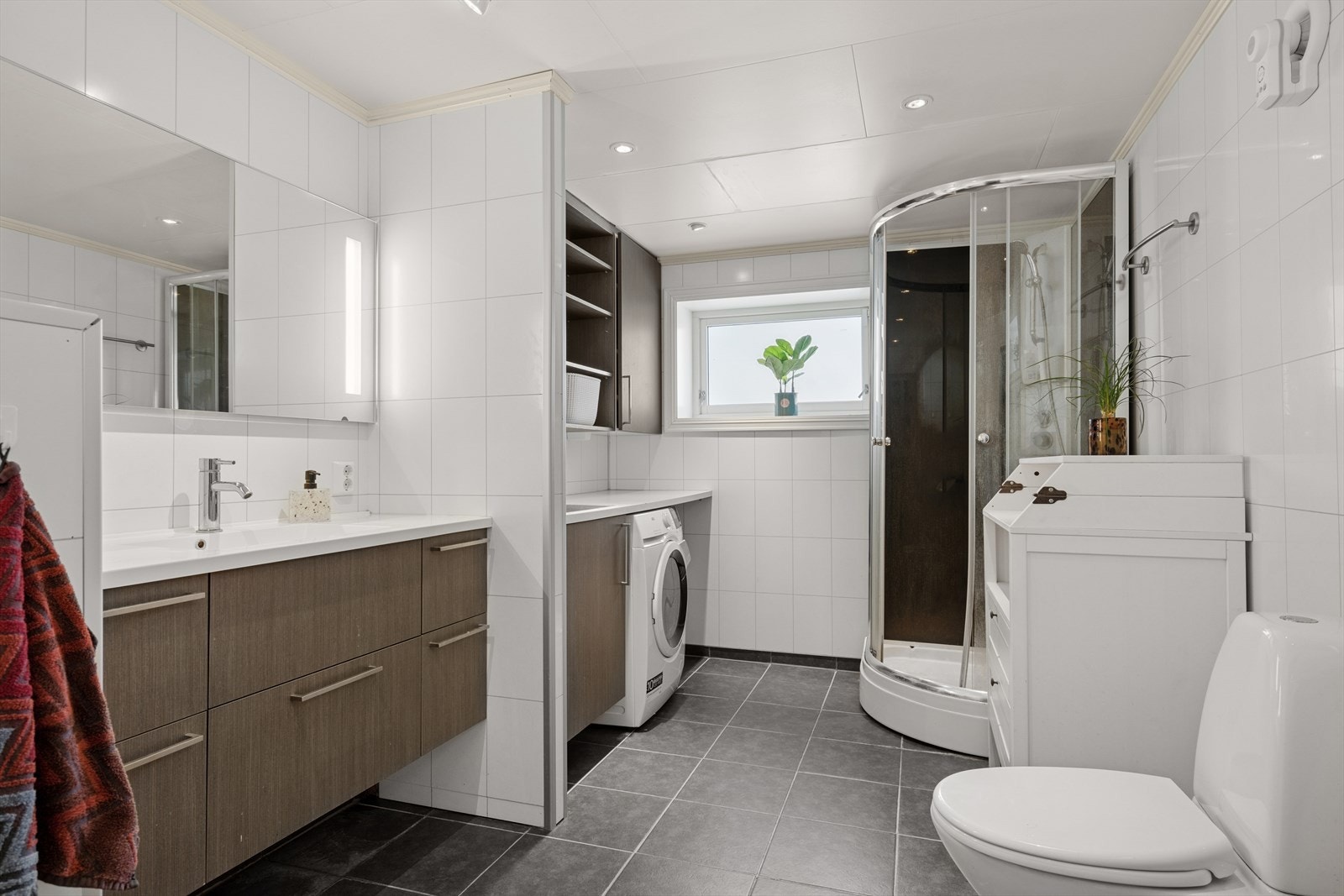 Badet er utstyrt med toalett, dusjkabinett, servant og speil med belysning. Opplegg for vaskemaskin med arbeidsbenk, servant og overskap. Galleribilde