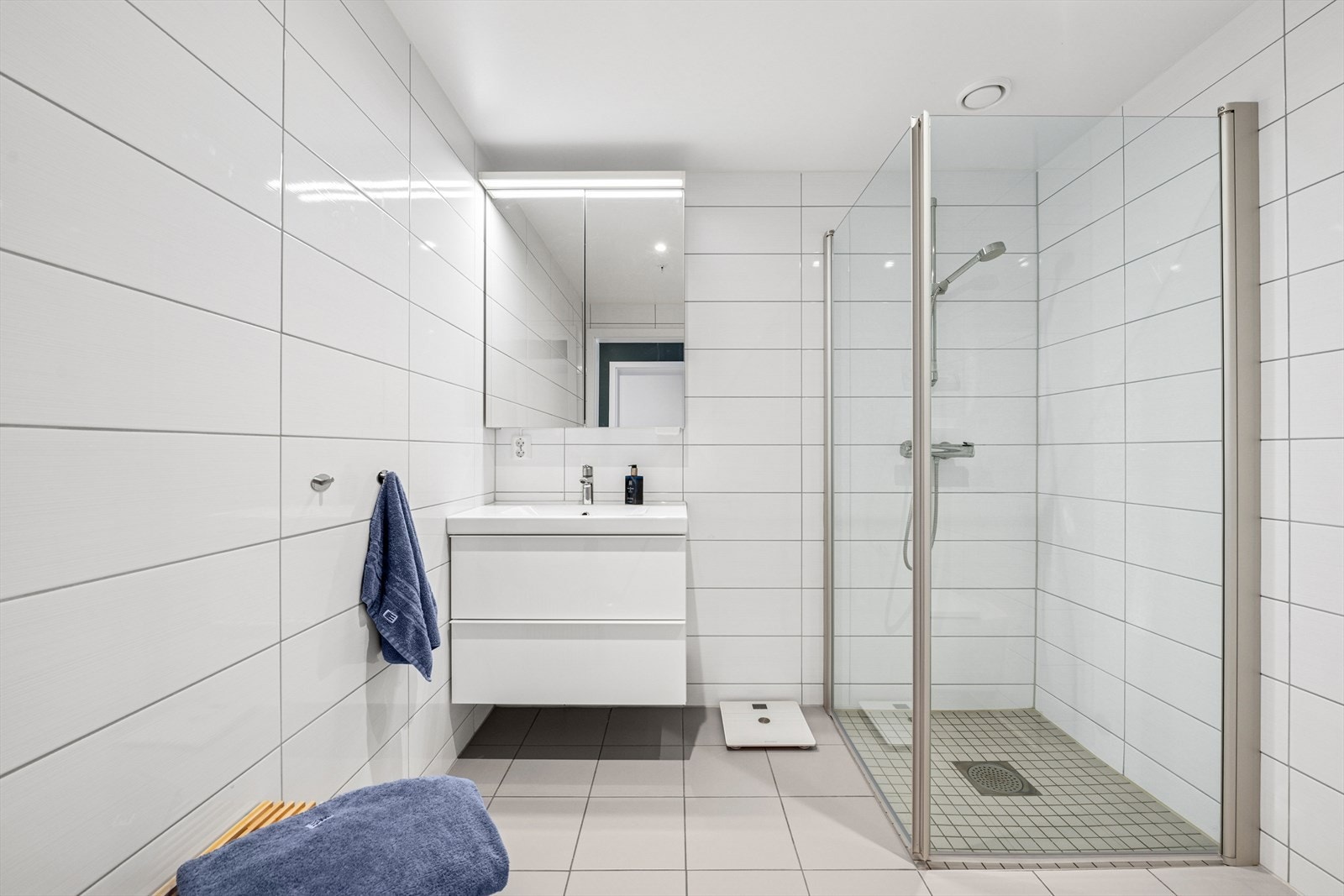 På dette badet er det montert en praktisk og stilfull baderomsinnredning med servant og skuffseksjoner, vegghengt toalett og speilskap med overbelysning. Romslig dusjsone med glassdører og pen spotbelysning i taket. Galleribilde