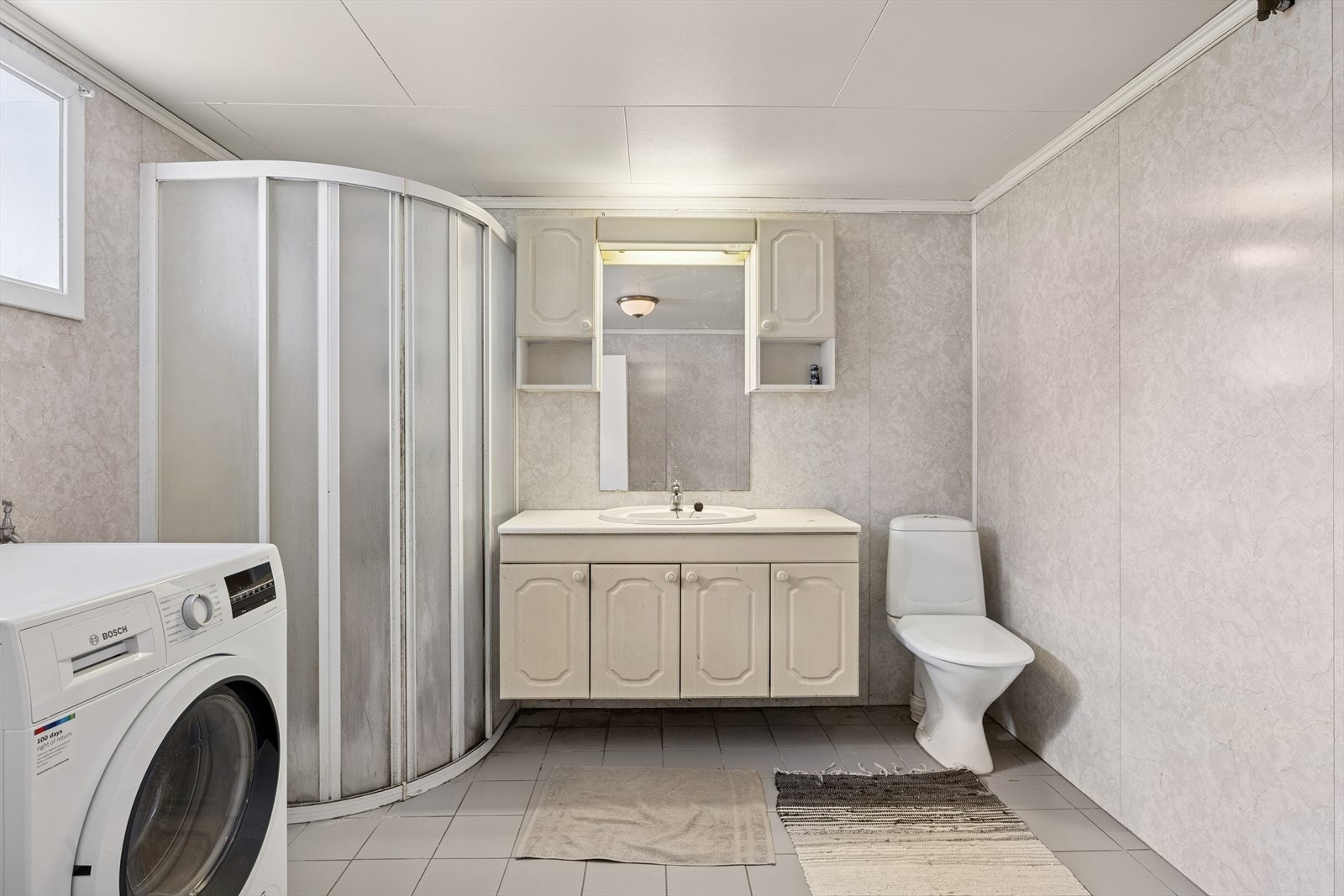 Badet er av eldre dato og har flislagt gulv med fall mot sluk. I dusjsonen er det utettheter i skjøtene mellom platene, og det er registrert fukt i både gulv og nedre del av veggene. Galleribilde