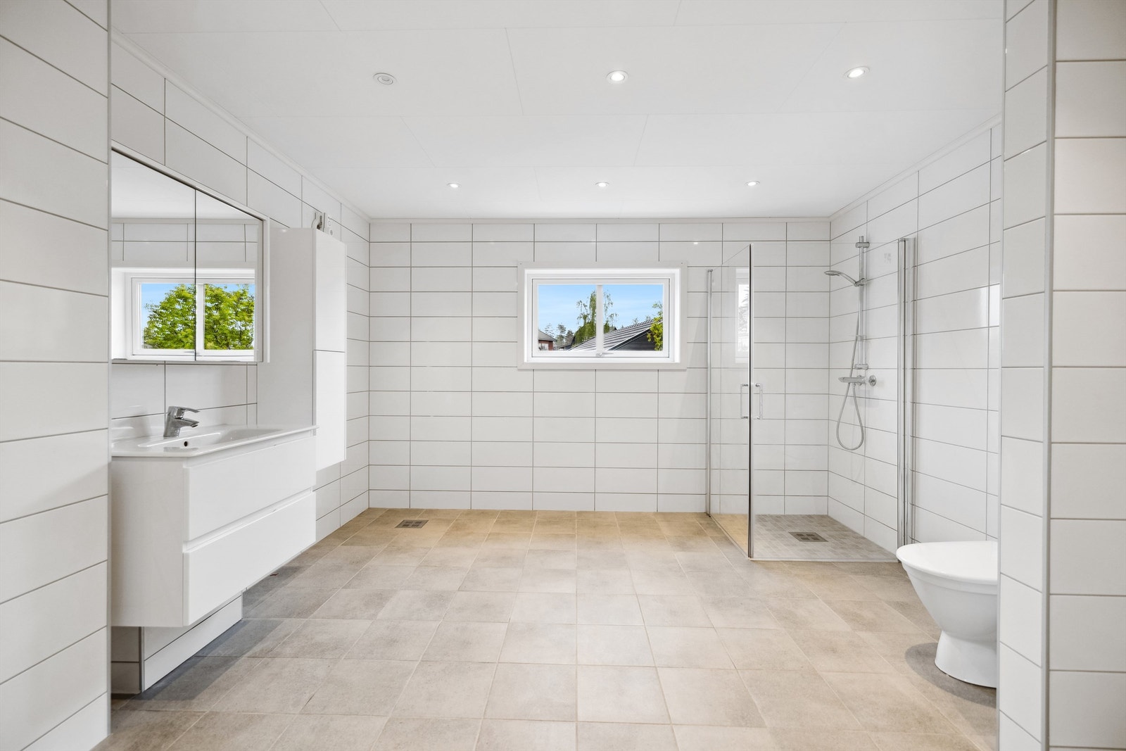 Stort bad fra 2020 med grå fliser på gulv med gulvvarme, hvite fliser på veggene og downlights i himling. Galleribilde