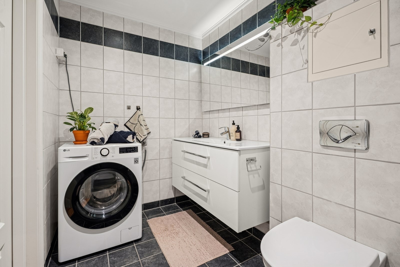 Rommet er innredet med servant med skap, vegghengt WC, opplegg for vaskemaskin og en avgrenset dusjsone med skyvedør. Galleribilde