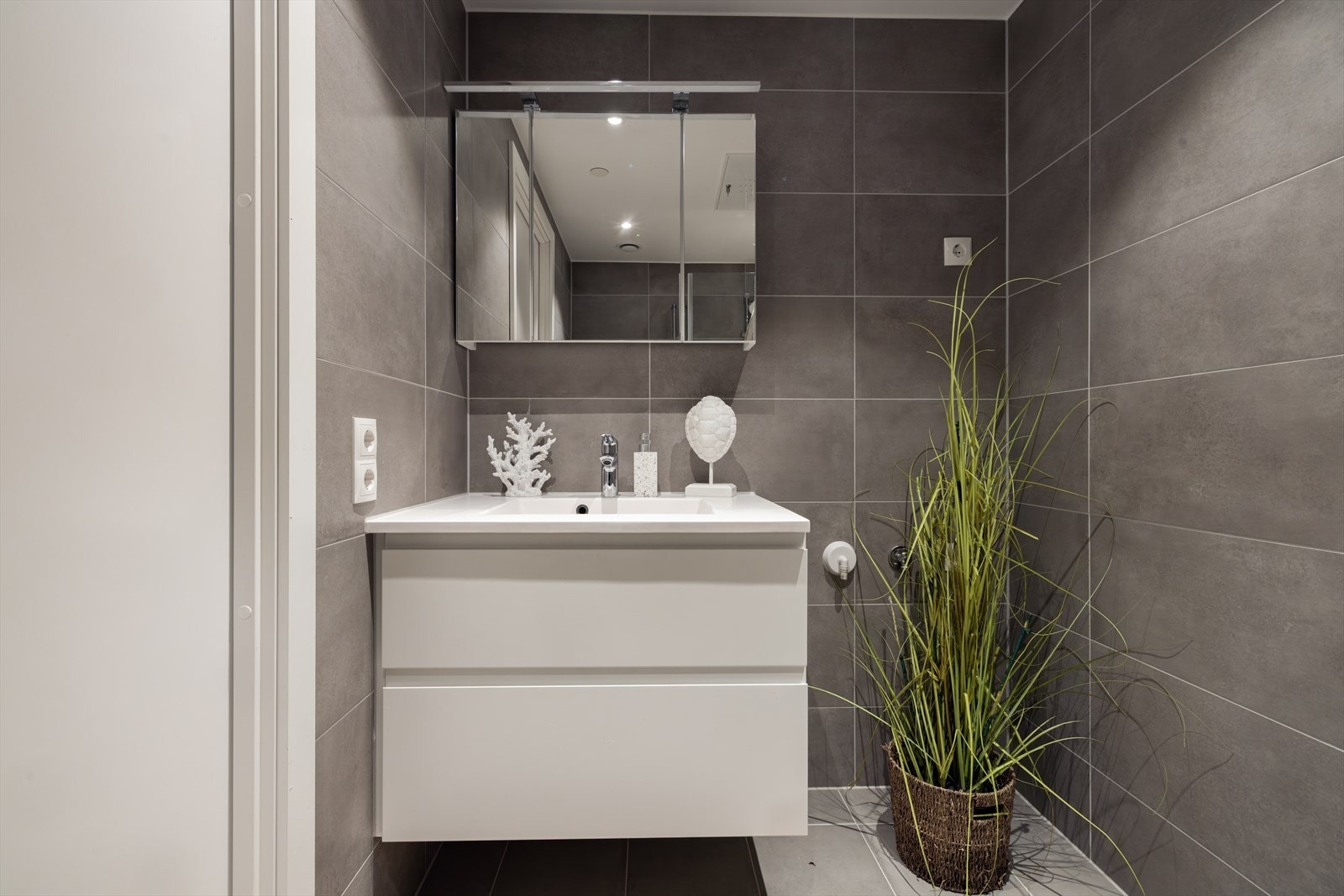 Downlights i himlingen gir godt lys, og innredningen består av hvite, glatte fronter med heldekkende servant på underskap og et stort speil med integrert belysning. Galleribilde