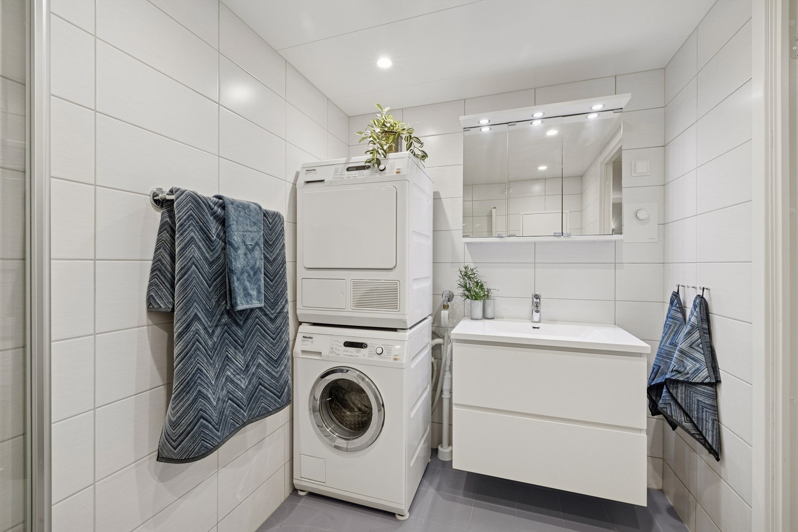 Baderomsinnredning med hvite, glatte fronter med romslige skuffer og heldekkende servantplate. Opplegg for vaskemaskin. Galleribilde