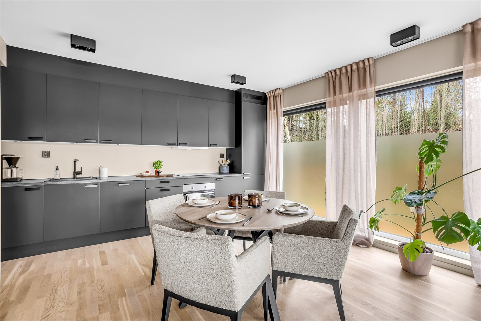 Innredningen består av mørke/glatte fronter, grå benkeplate med laminatbelegg, sorte håndtak på dører/skuffer, lys under overskap og sort vask. Galleribilde