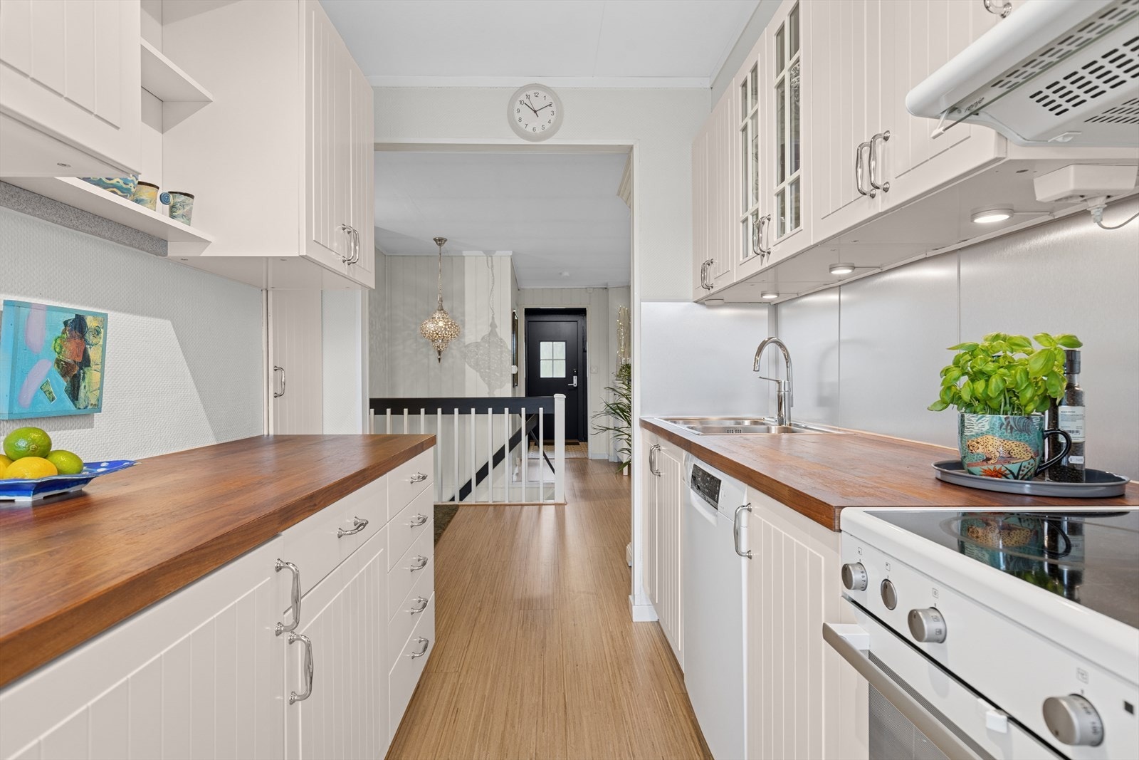 Lys og tidløs kjøkkeninnredning med profilerte fronter og finerte benkeplater. Det er benkebelysning under overskapene. Galleribilde