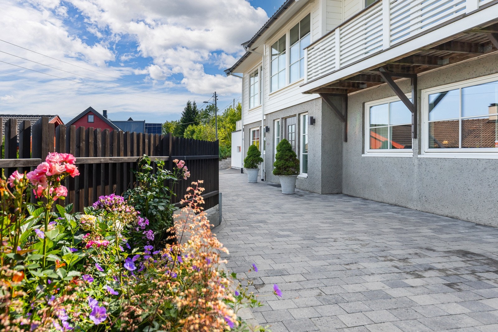 Pent opparbeidet gårdsplass med belegningsstein, blomstrende bed og hyggelig inngangsparti. Galleribilde