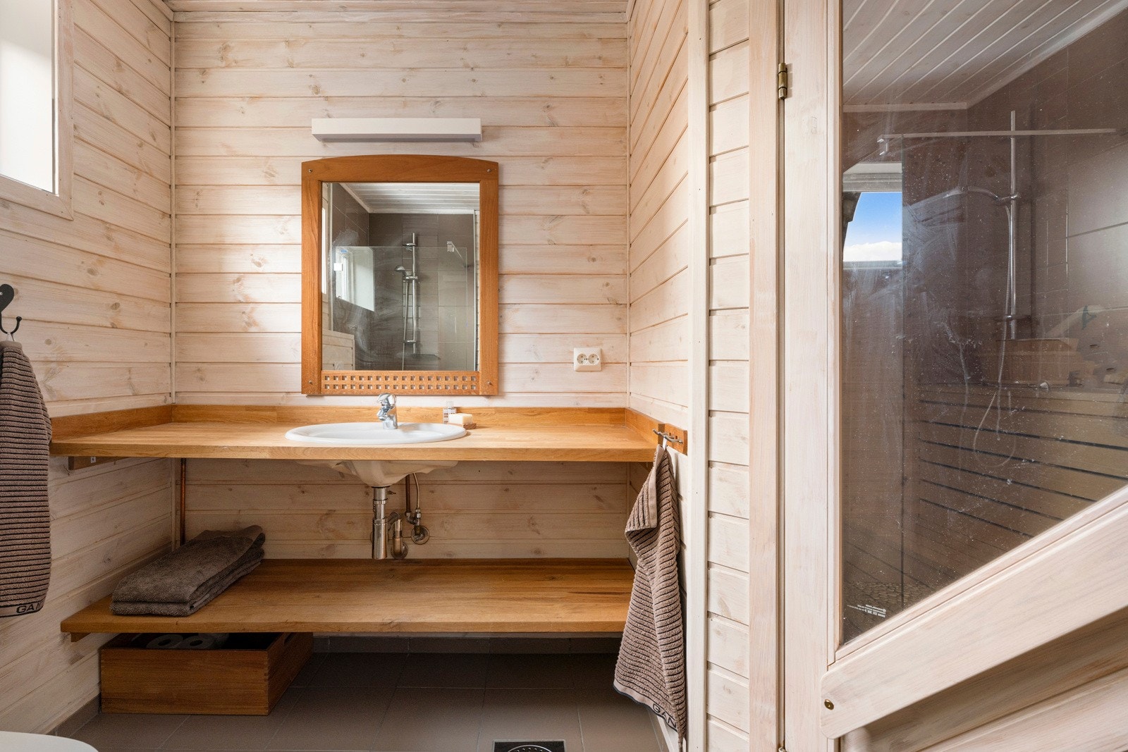 Badet har et delikat uttrykk, der store, grå gulvfliser kombineres med trepanel og matchende fliser på veggene Galleribilde