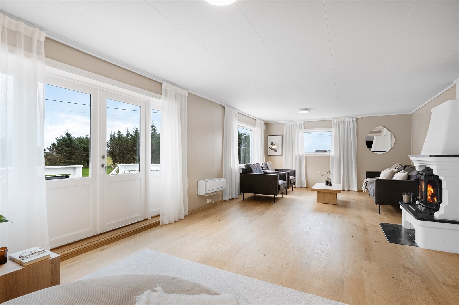 Flott lys stue med enstavs parkett på gulv, varmepumpe og flott vedovn. Galleribilde