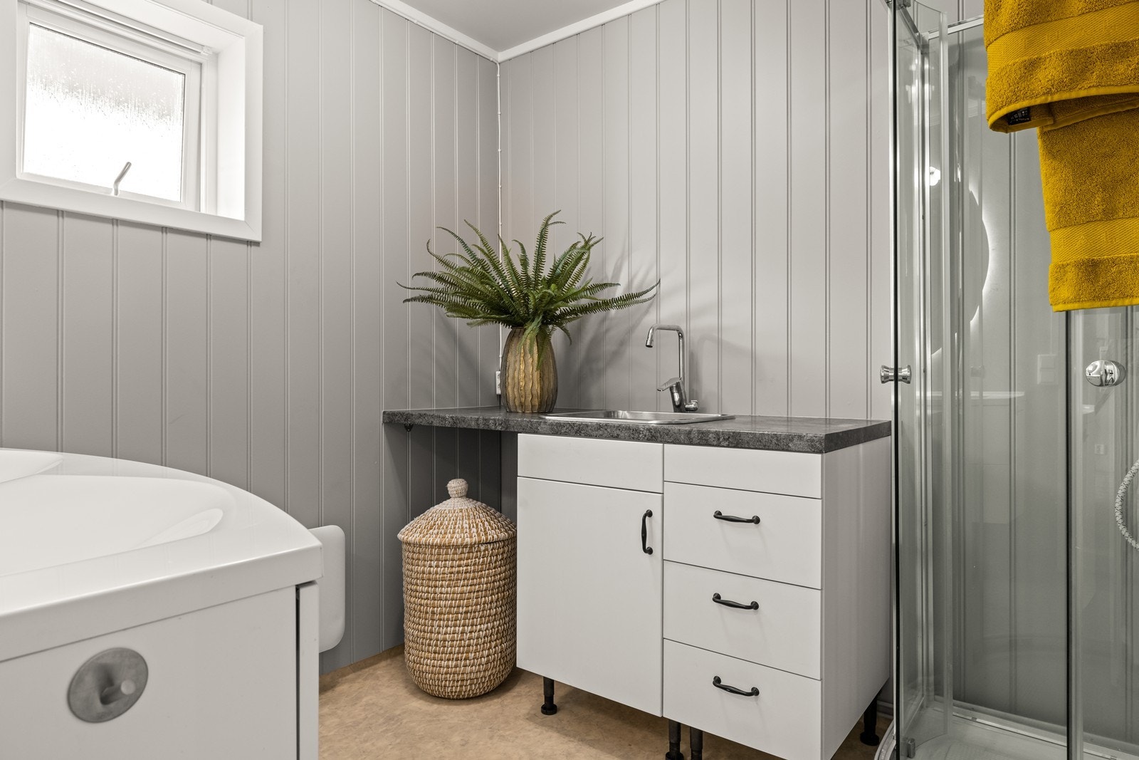 Gulvet på bad har vinylbelegg med oppbrett, som sikrer god vannmotstand.
Rommet er innredet med to nedfelte servanter, dusjkabinett, og utslagsvask, samt opplegg for vaskemaskin - alt tilrettelagt for en effektiv hverdag. Galleribilde