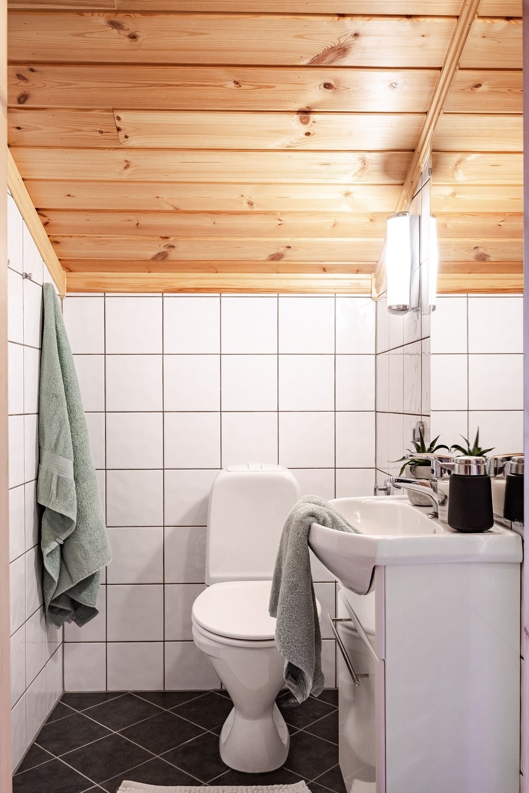 Baderommet har mørke fliser på gulv med elektrisk gulvvarme og er utstyrt med servantinnredning, dusjnisje og gulvstående toalett. Galleribilde