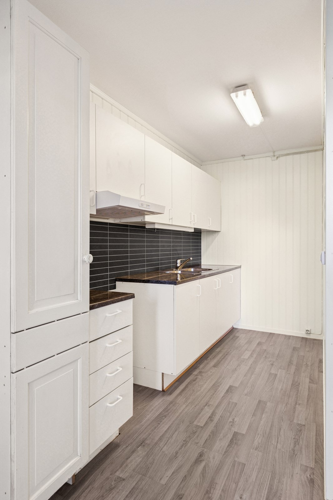 Videre er kjøkkenet utstyrt med laminert benkeplate med oppvaskkum og plater på vegg over benkeplate. Galleribilde
