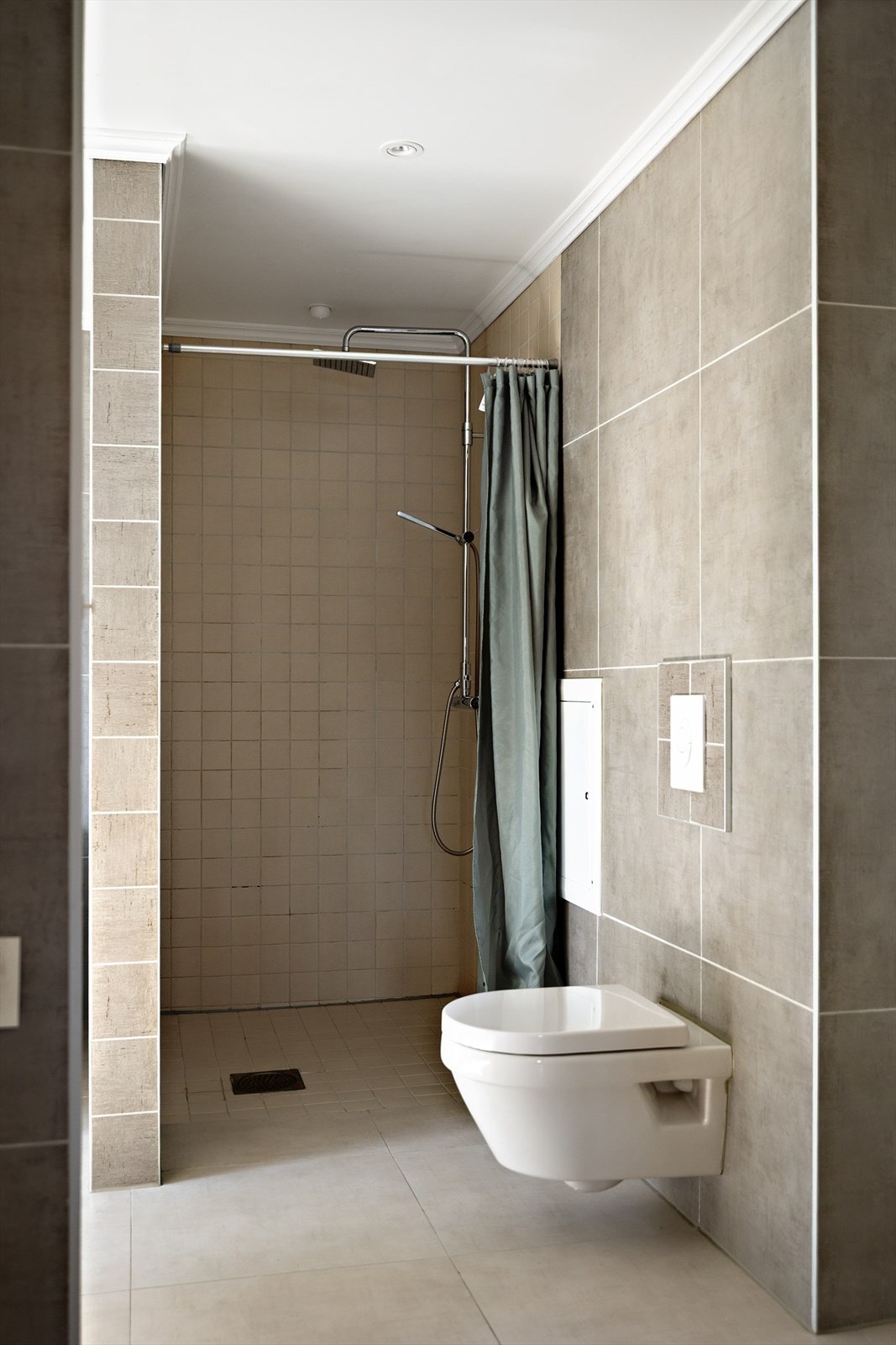 Fliser på både gulv og vegger gir et tidløst og stilrent uttrykk, mens taket med malte plater og innfelte downlights gir en lun belysning og en moderne atmosfære. Galleribilde