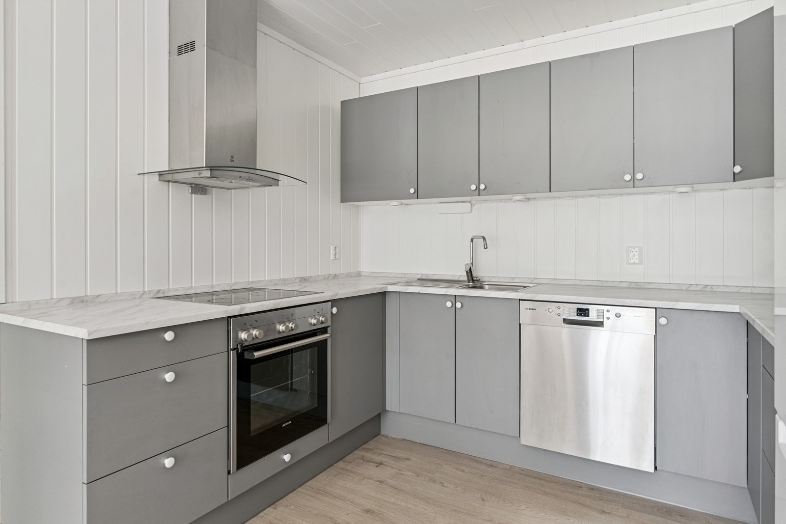 Kjøkkeninnreiing frå JKE med glatte, grå frontar montert i åpen løysing mot stove i underetasje Galleribilde