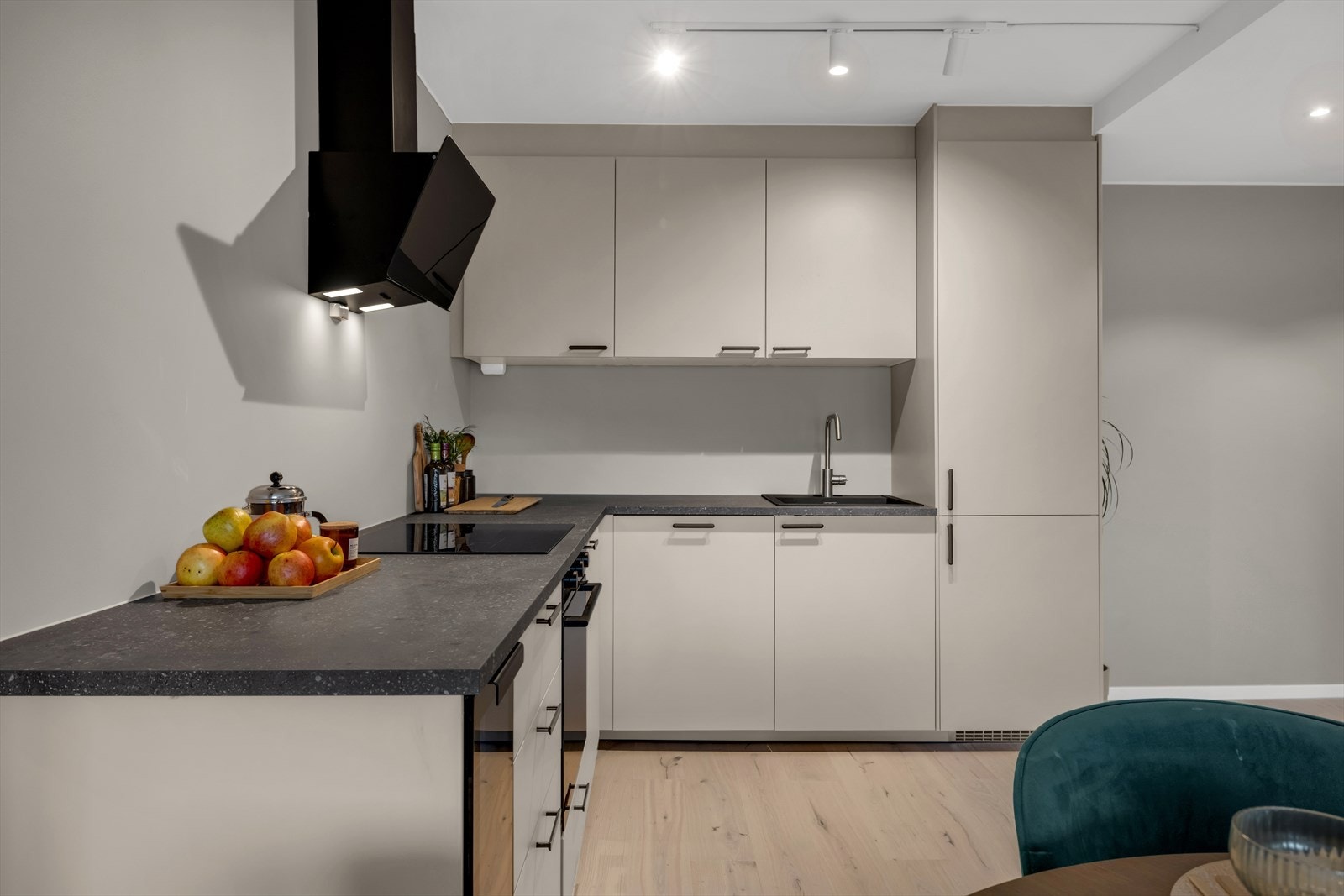 Kjøkkenet fra 2025 har et stilrent design med lyse, glatte fronter, laminat benkeplate med nedfelt vaskekum og kontrasterende mørke detaljer. Galleribilde