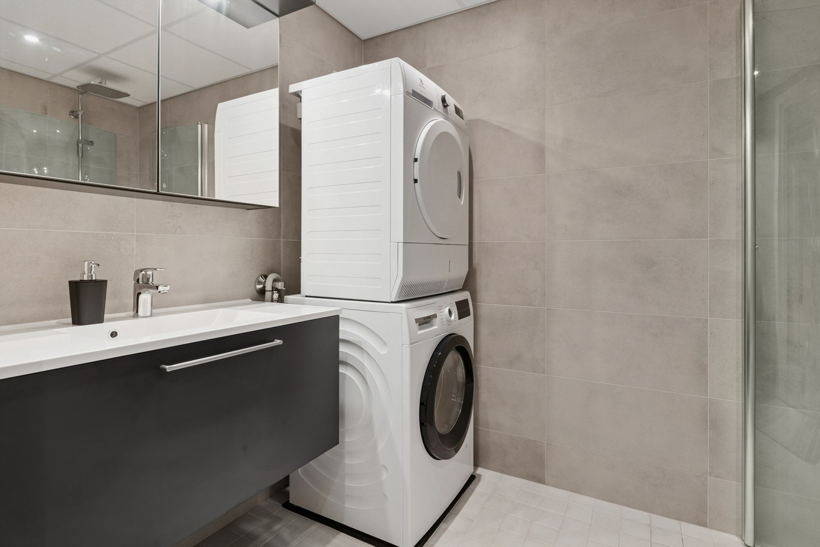 Rommet har en stilren, moderne innredning, opplegg for vaskemaskin, innfellbare dusjdører i glass, lun gulvvarme og innfelt spotbelysning i himlingen. Galleribilde