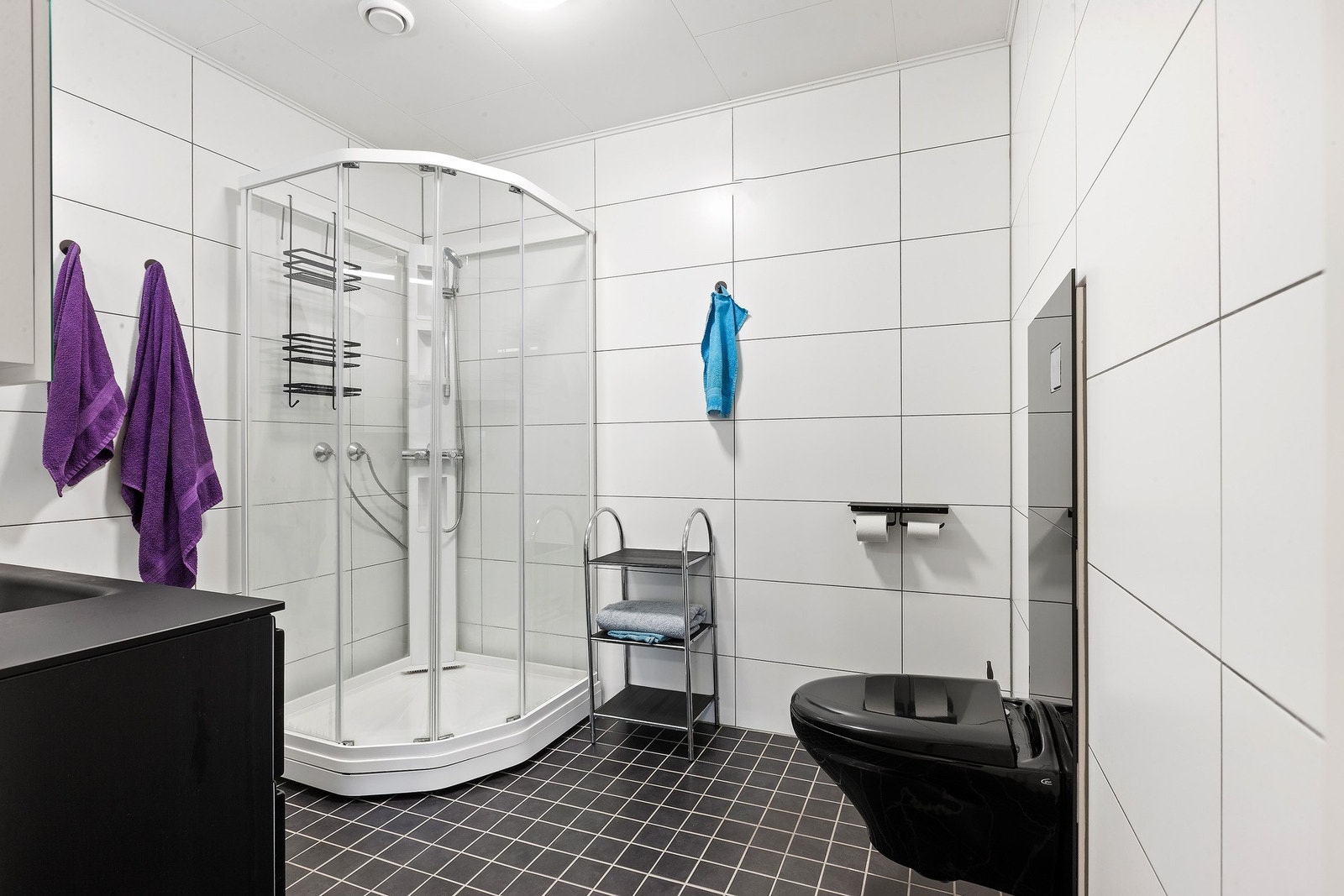 Badet har mørk innredning med skuffer under, speilskap med lys over, dusjkabinett og vegghengt toalett. Galleribilde