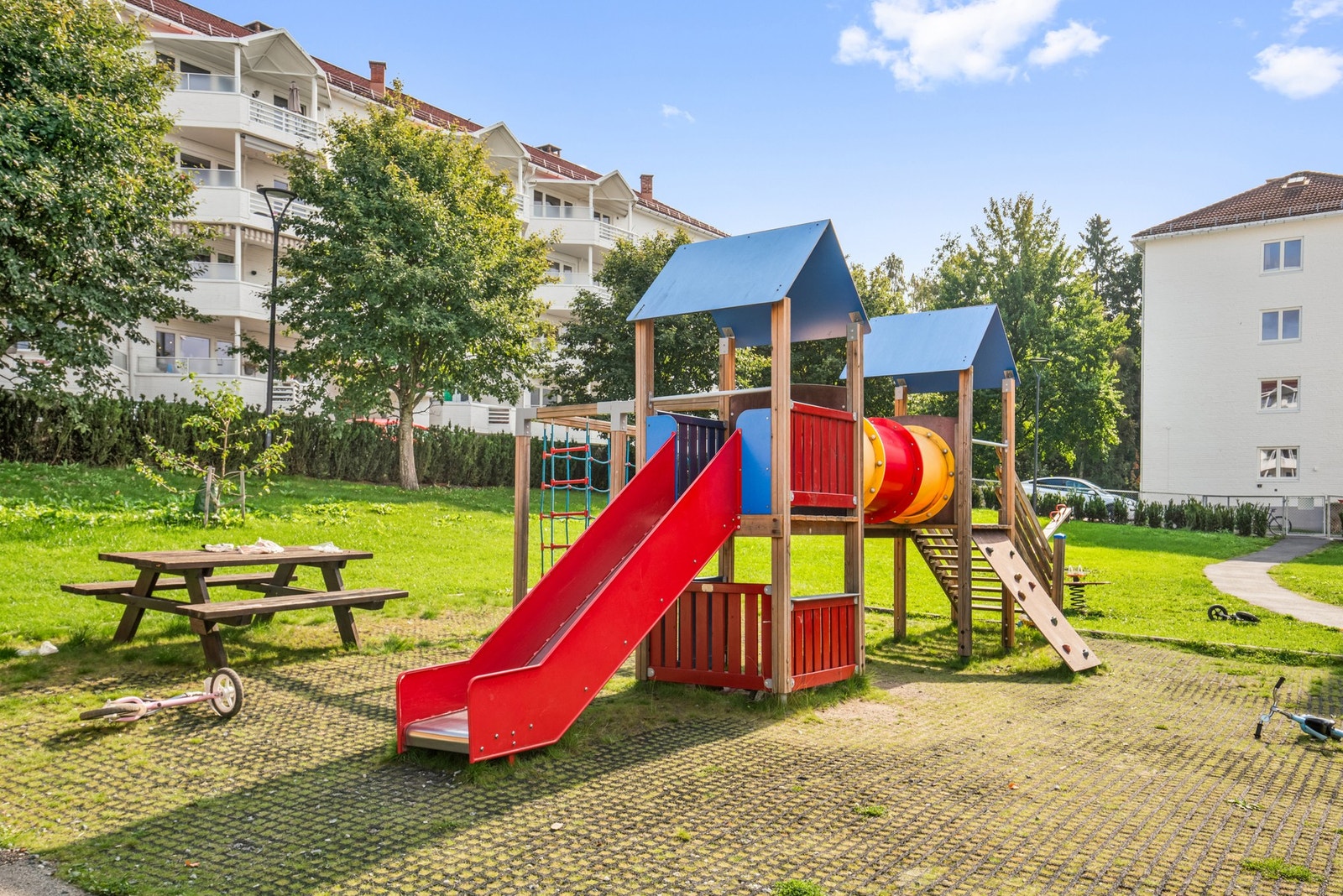 Fellestomten er grønn og solrik, med boltreplass, lekeapparater og sittebenker. Galleribilde