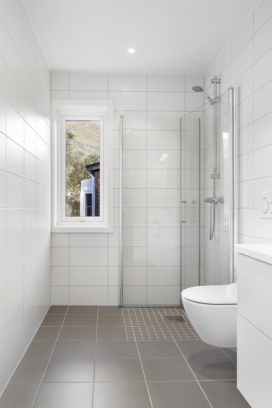 Badet er innredning med nedfelt servant, speilskap med lys over, veggmontert toalett og innfellbare dusjvegger i glass. Galleribilde