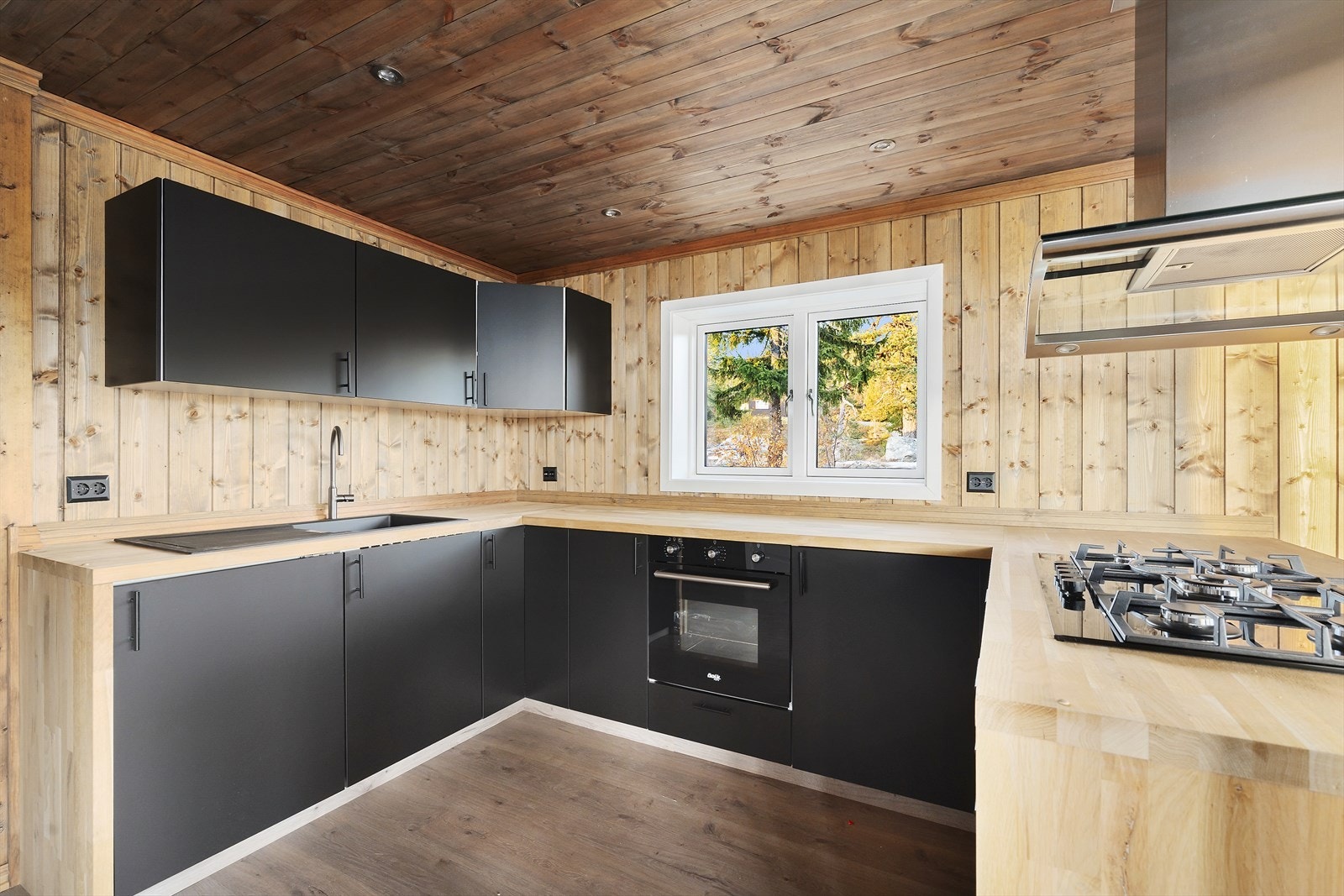 Stilrent kjøkken med moderne innredning i svart utførelse og heltre benkeplate som gir en lun kontrast. Galleribilde