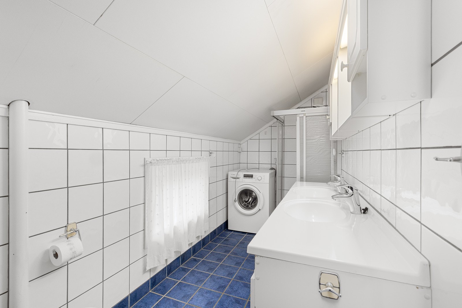 Rommet er innredet med skap med to nedfelte servanter, toalett, dusjhjørne med glassvegger og opplegg for vaskemaskin. Galleribilde