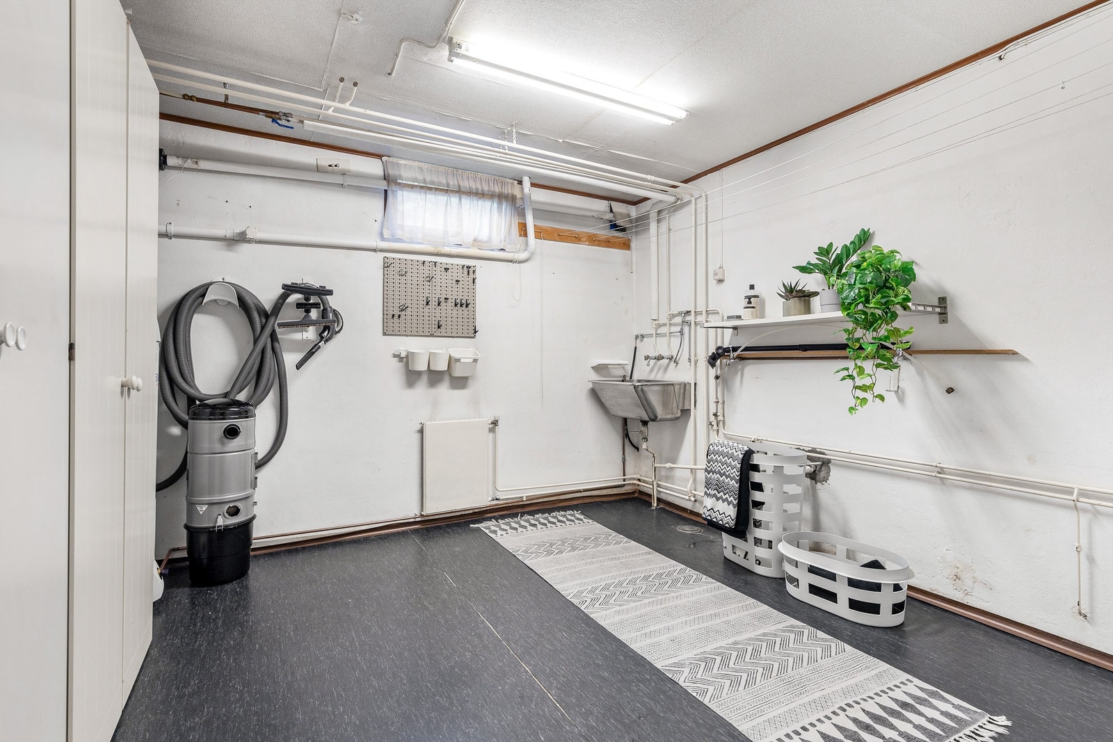 Gulvflate belagt med gulvbelegg. Vegger i malt mur. Himling med tapet. Vegghengt utslagsvask i rustfritt stål med to-greps armatur. Vanntilførsel til vaskemaskin. Gulvstående skap. Varmtvannsbereder på ca. 200 liter fra 2019 plassert i hjørnet. Galleribilde