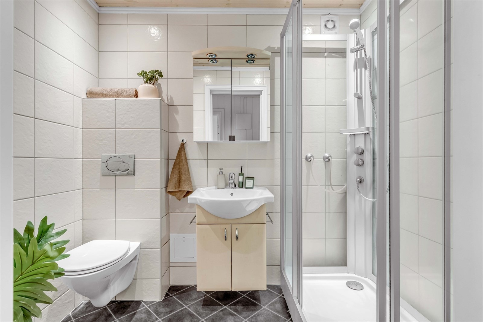 Hovedbadet er flislagt på både gulv og vegger, og innredningen består av vegghengt toalett, servant, speilskap og dusjhjørne. Galleribilde