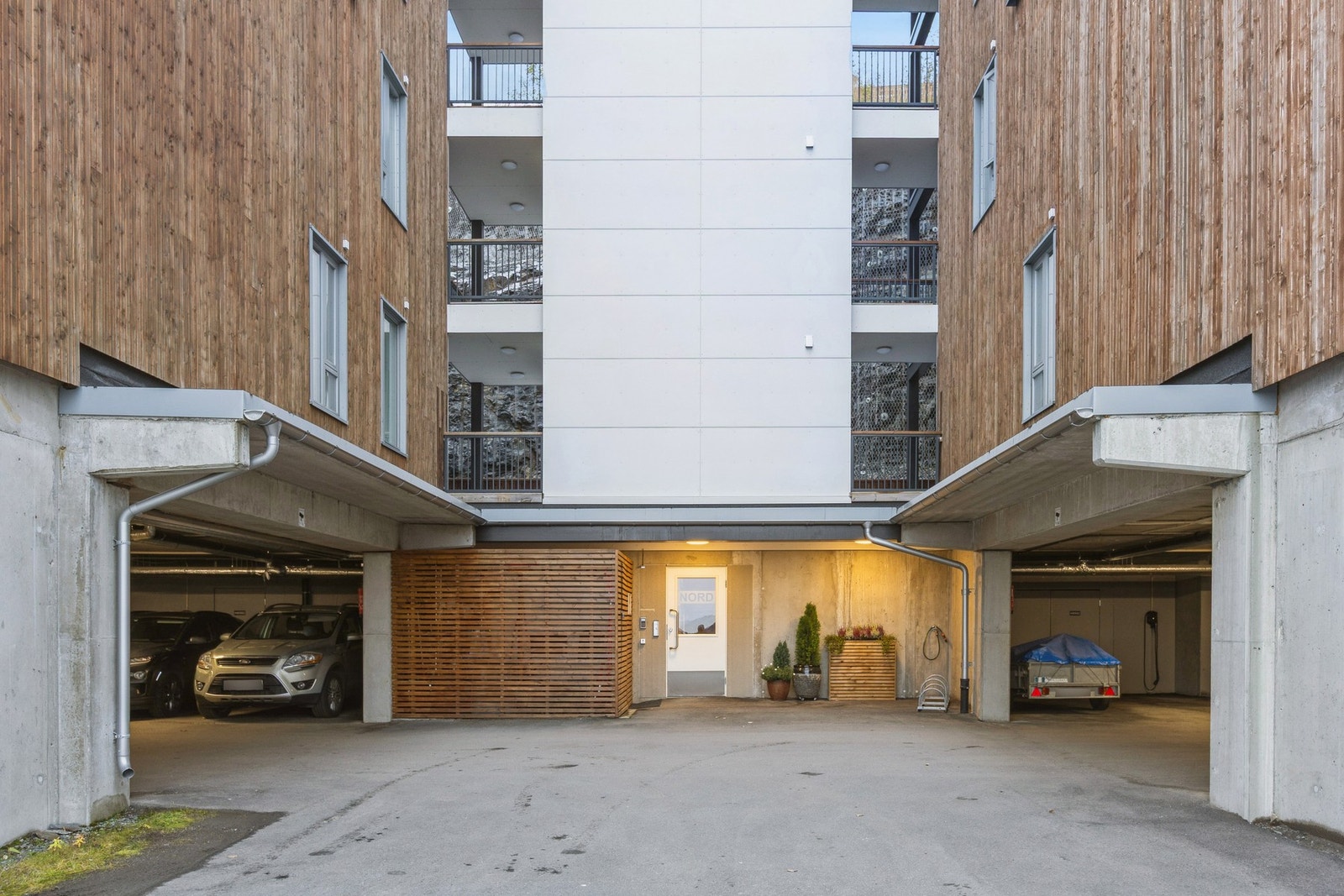 Ryddig inngangsparti med innkjøring til parkeringsanlegget hvor denne leiligheten har parkering til høyre. Galleribilde