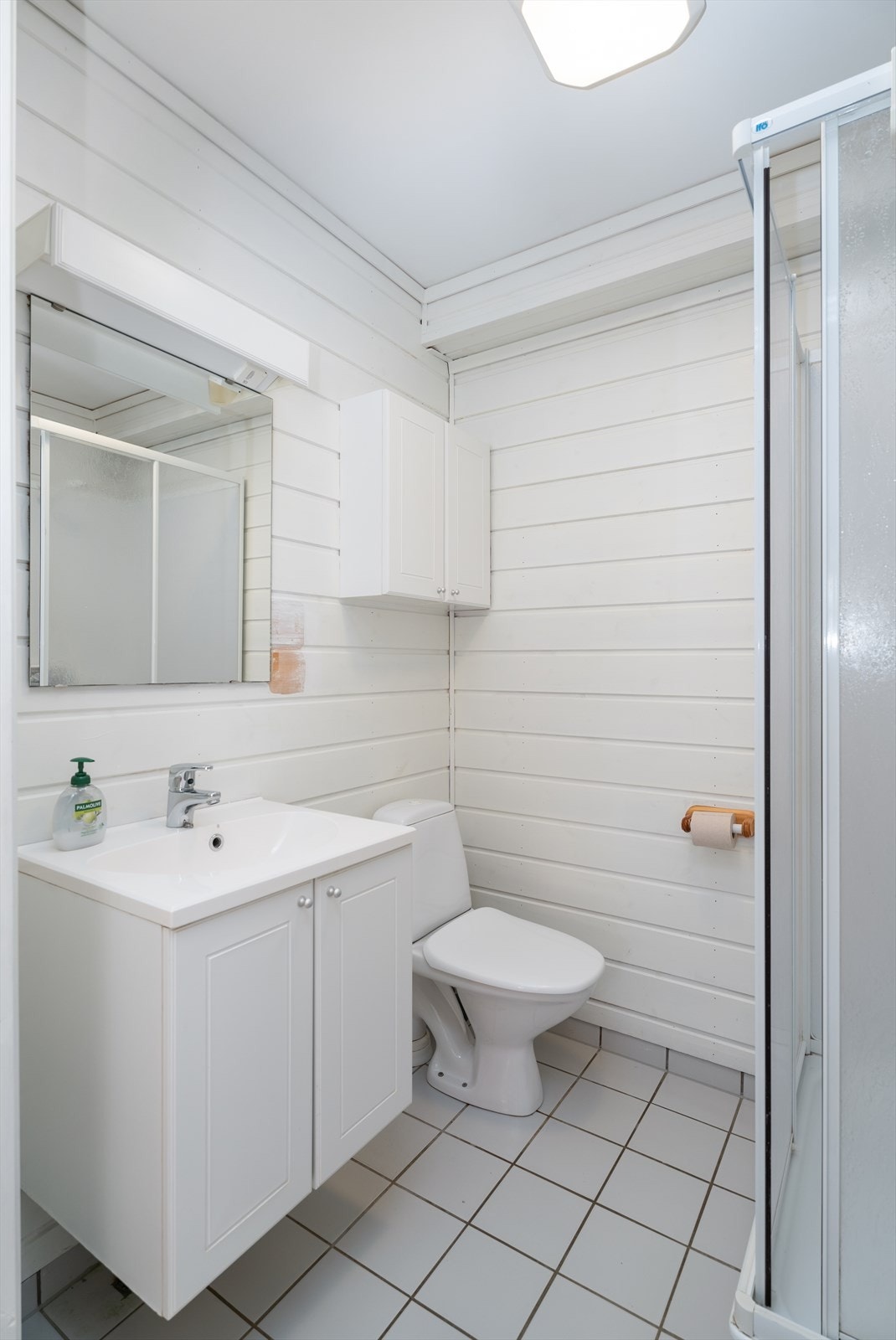 Baderom med fliser på gulv med varmekabler. Enkelt baderomsinnredning, toalett og dusjkabinett. Galleribilde