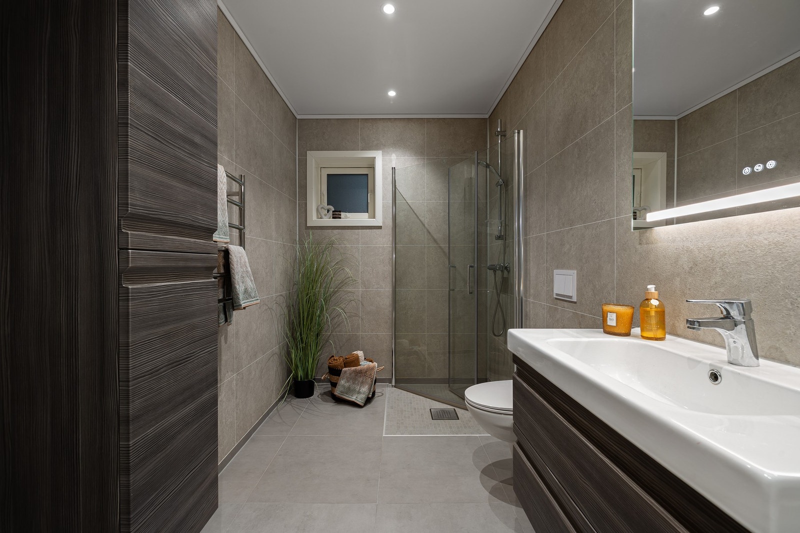 Badet er utstyrt med opplegg for vaskemaskin, mekanisk avtrekk, servant, servantskap, innfellbare dusjdører og veggmontert wc. Galleribilde